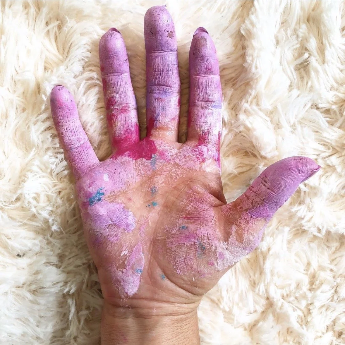 Photograph of the hand of Artist Dana Savoca Tietze covered in paint in tones of pink, purple and blue