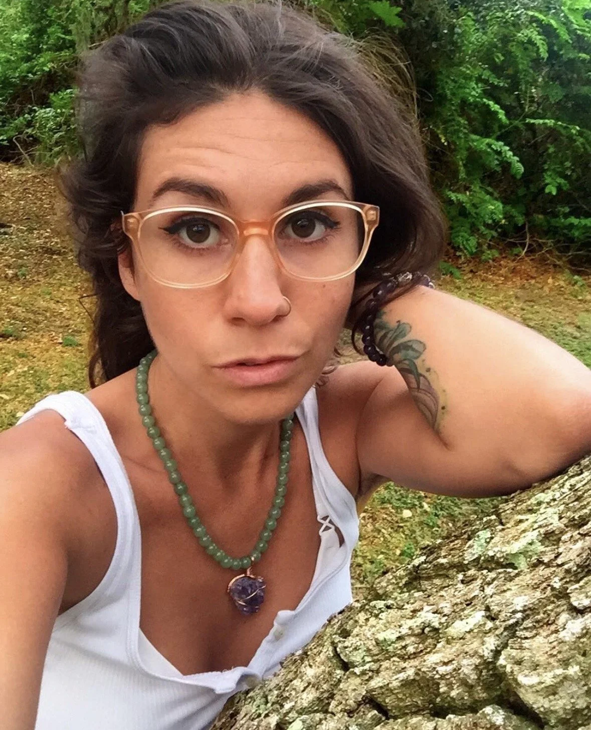 Artist Dana Savoca Tietze wearing a large beaded amethyst pendant necklace is perched on a tree