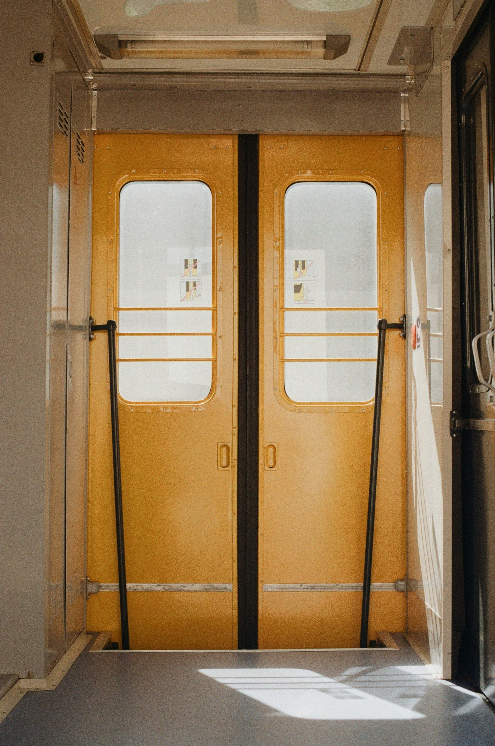 Yellow train doors with windows and safety warnings, opened inside a train station or transit vehicle.