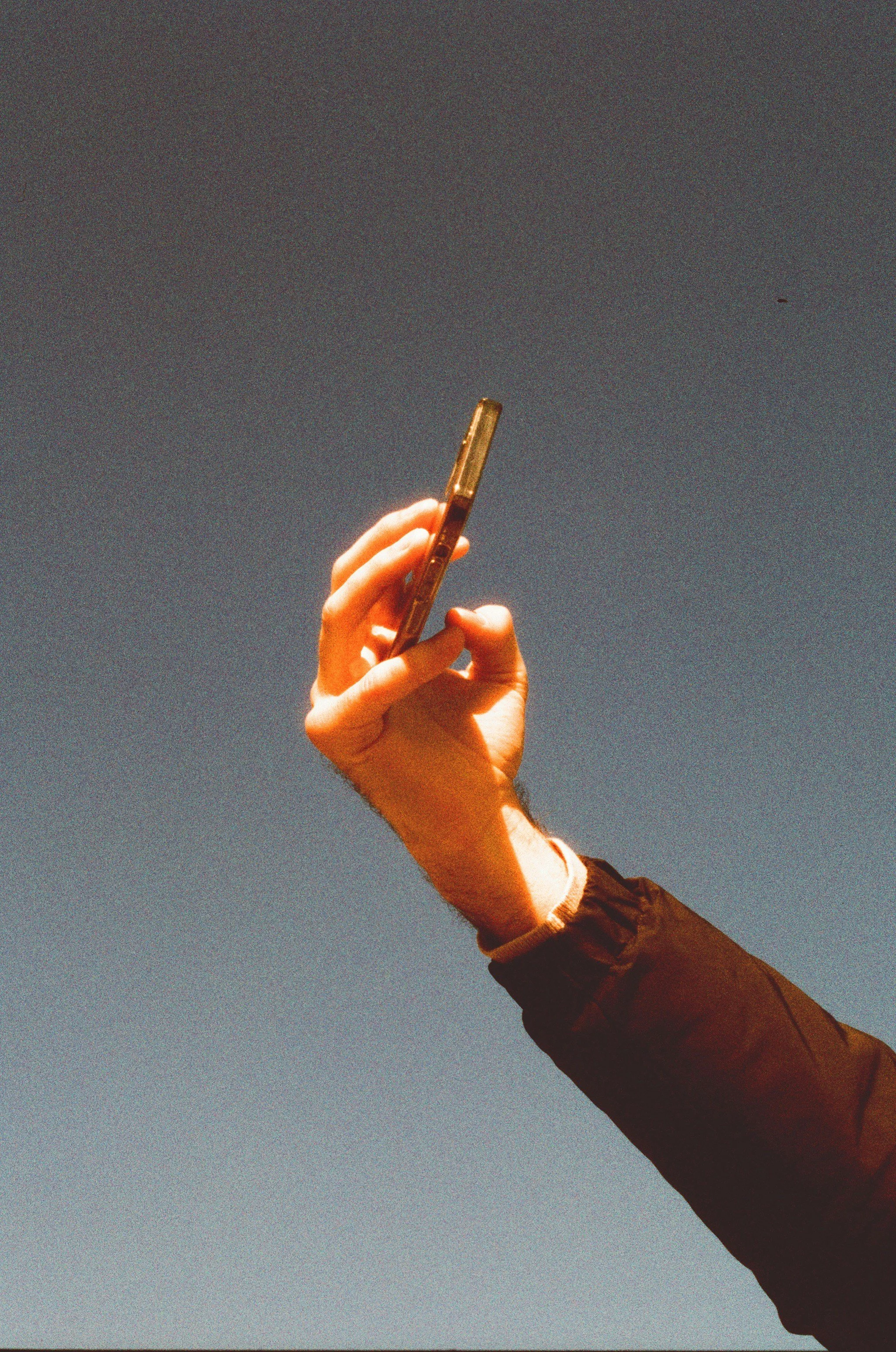 A person holding a smartphone in their right hand against a clear blue sky