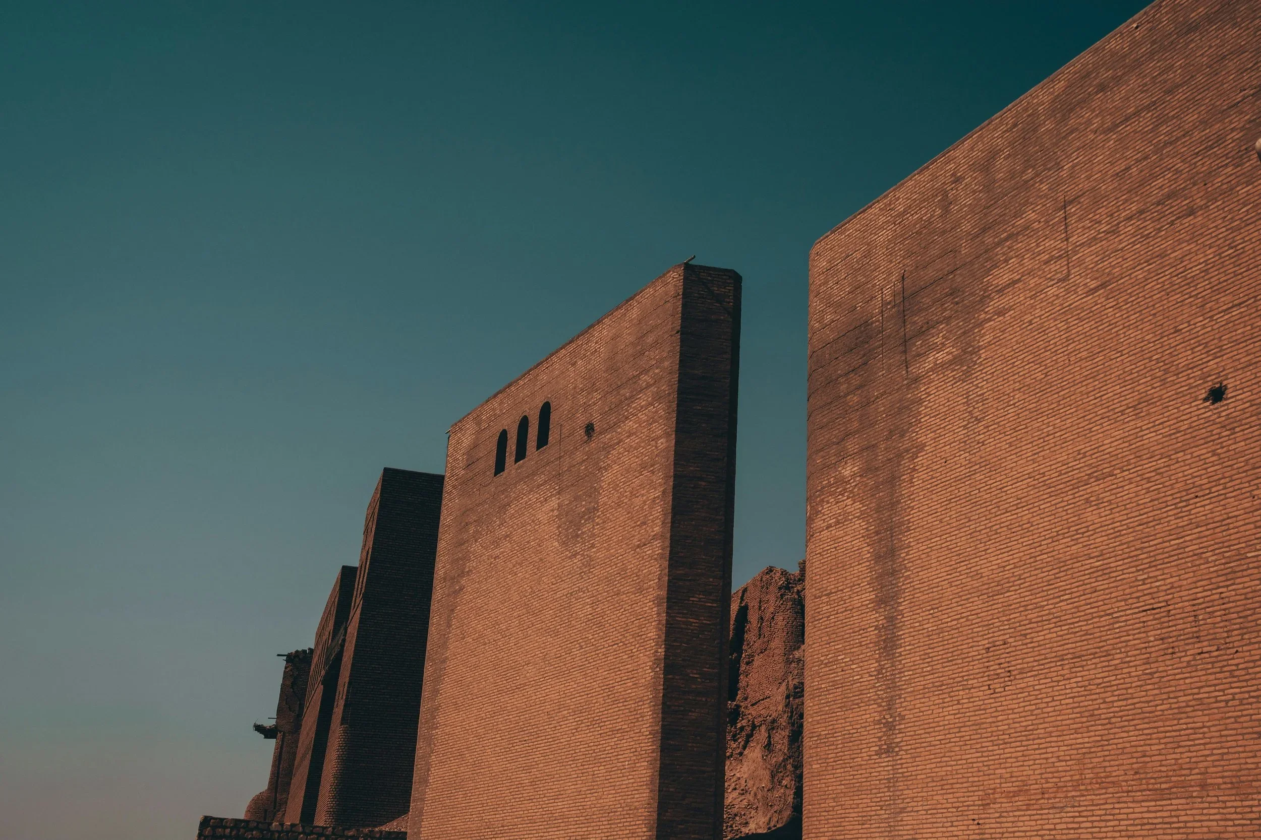 A photograph of tall brick buildings against a clear blue sky, with shadows cast on the brick facades.