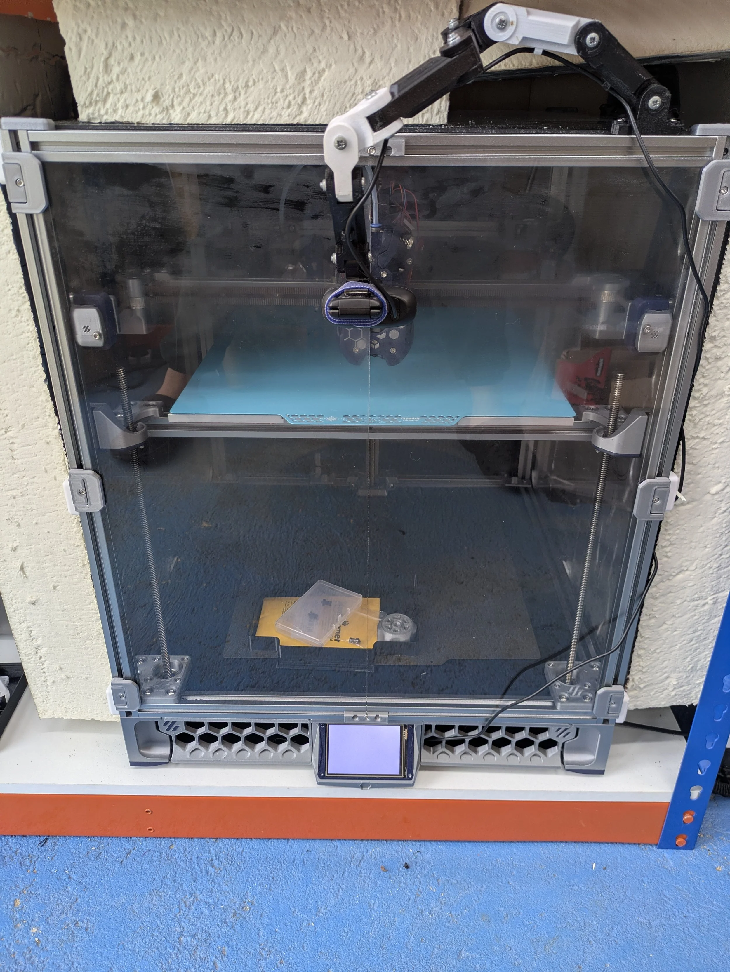 A 3D printer on a blue and orange workbench with a red floor in the background.