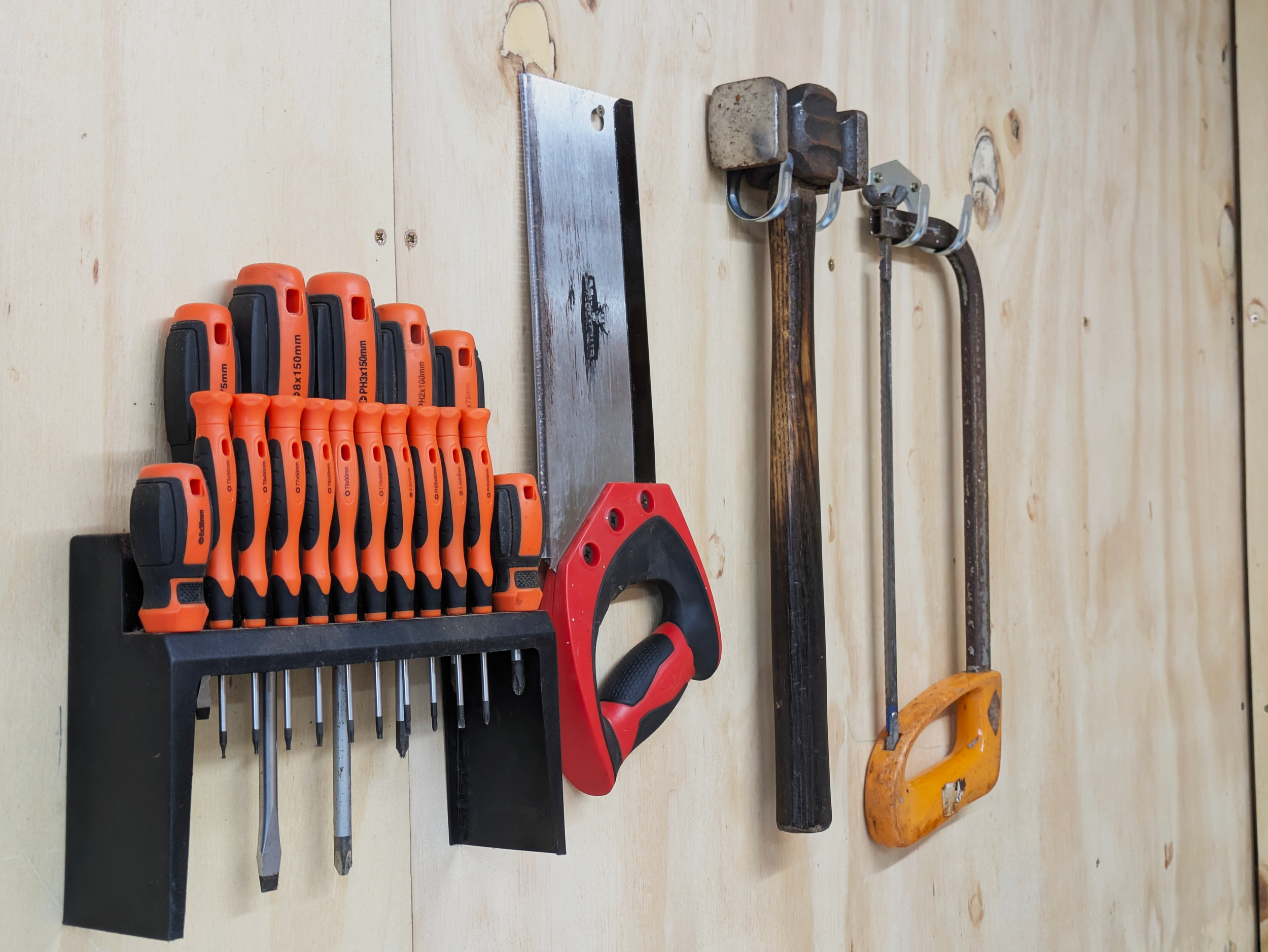 A wall-mounted organization of various hand tools including screwdrivers, a saw, a hammer, a wrench, and a hacksaw.