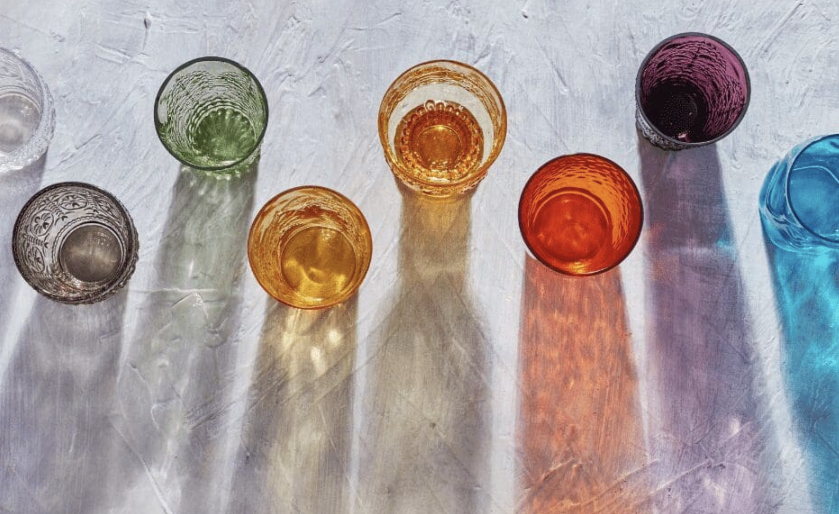 Colorful glass cups casting colorful shadows on a textured white surface.