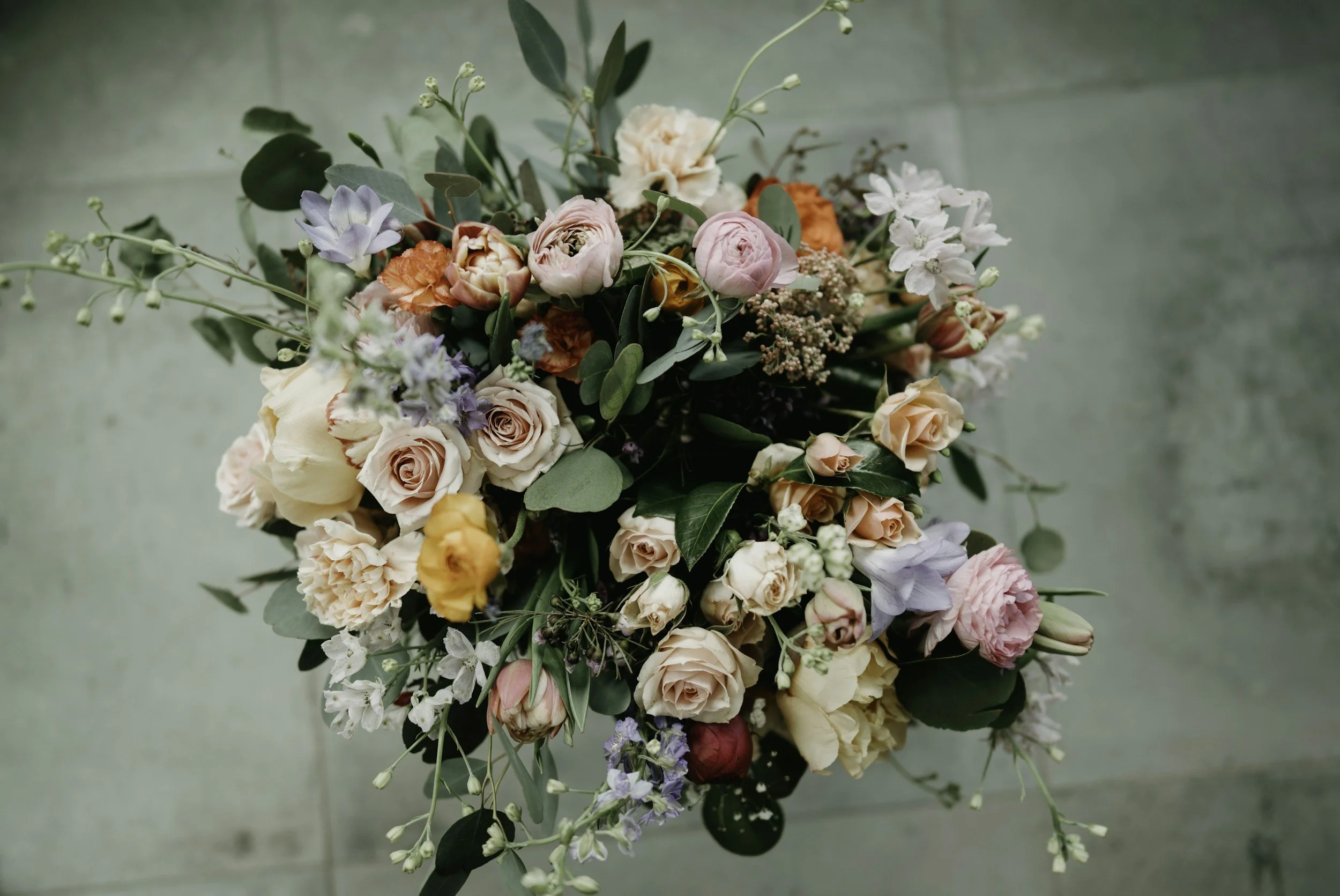 A colorful bouquet of various flowers including roses, peonies, and other mixed flowers with green leaves on a greenish floor.