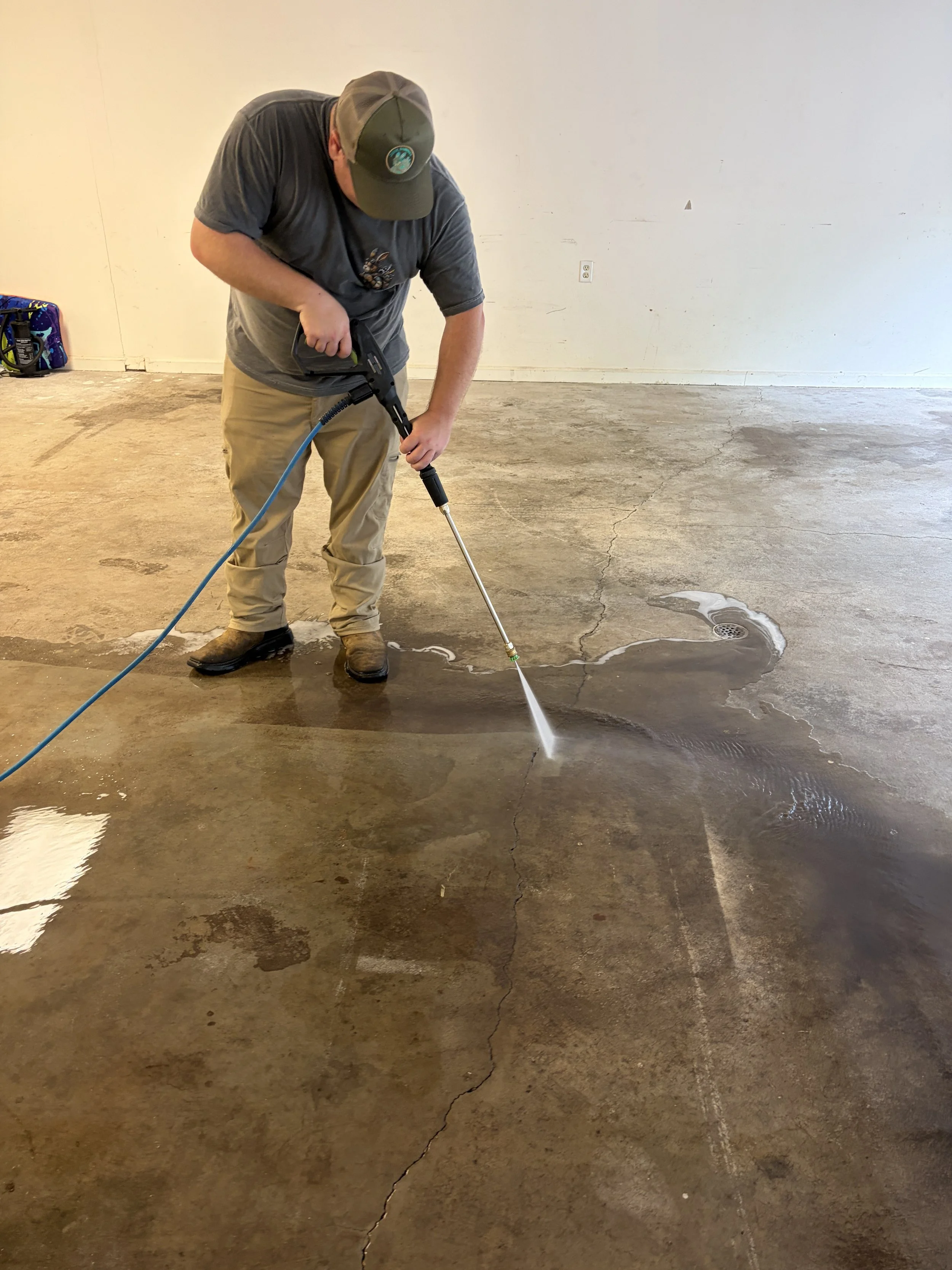 Man using a pressure washer on a cracked concrete floor in an empty room.