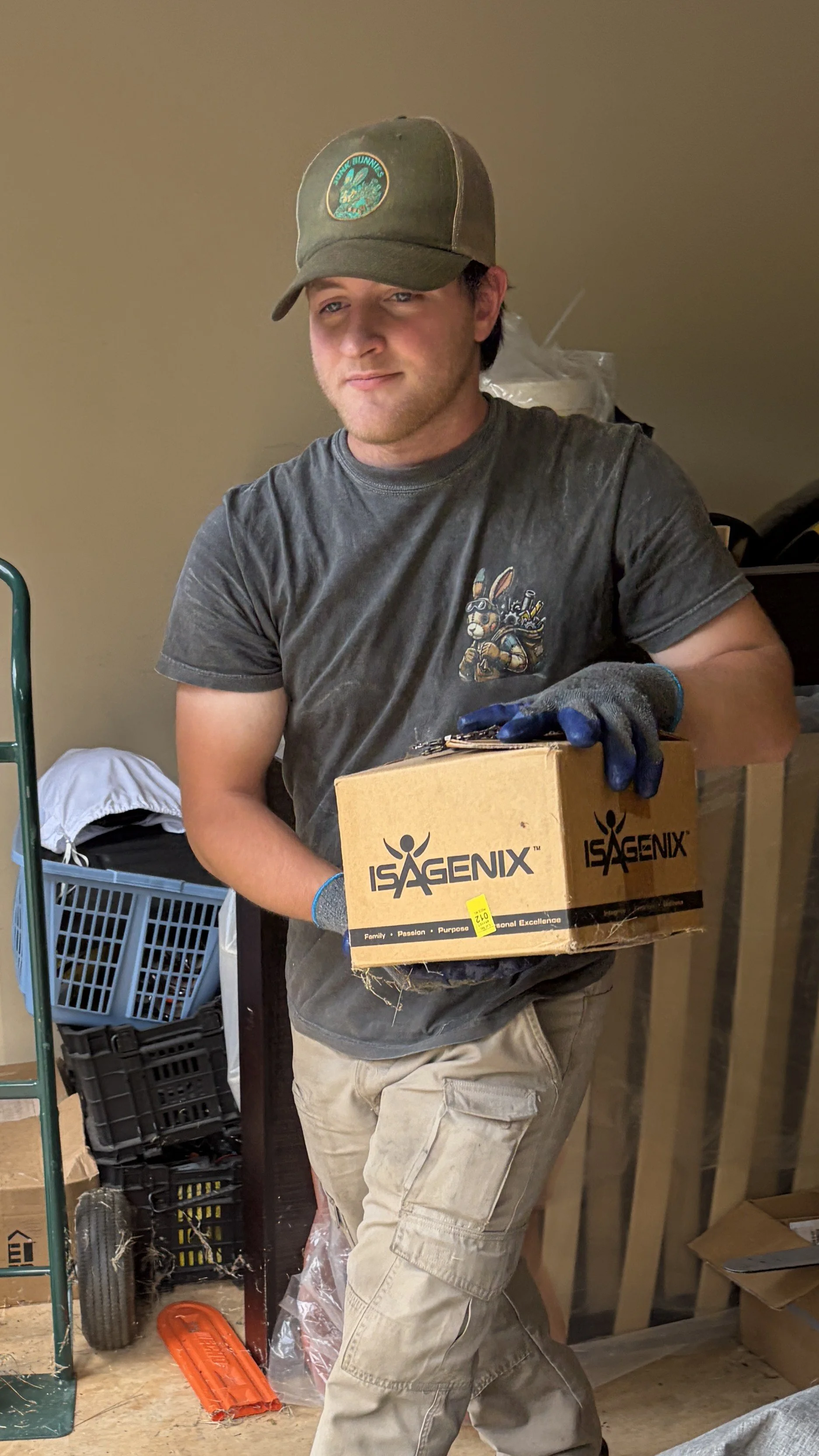 Co-Owner of Junk Bunnies LLC Michael Outman wearing a gray T-shirt, cargo pants, blue gloves, and a green baseball cap Removing Junk from a recent job.