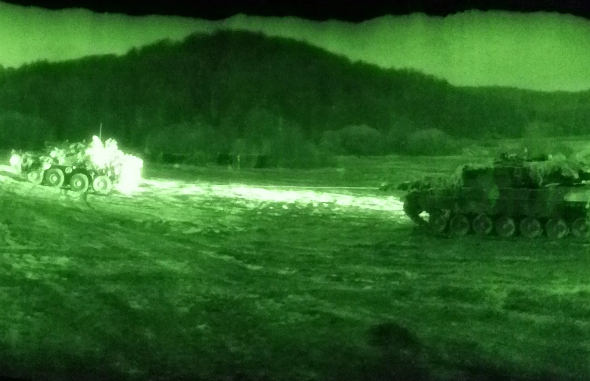 Night vision photo showing two military tanks in a field with mountains in the background.