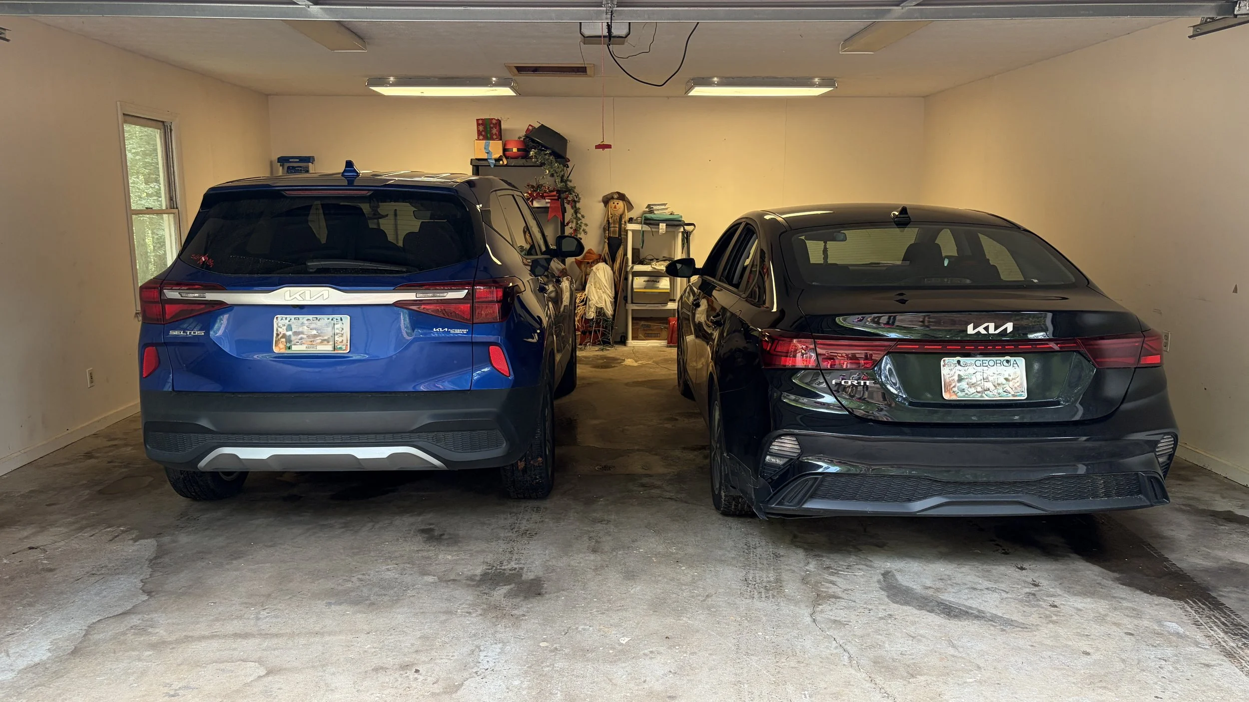 a Clean organized Garage with two parked cars, a blue SUV and a black sedan, with holiday decorations and storage shelves in the background.