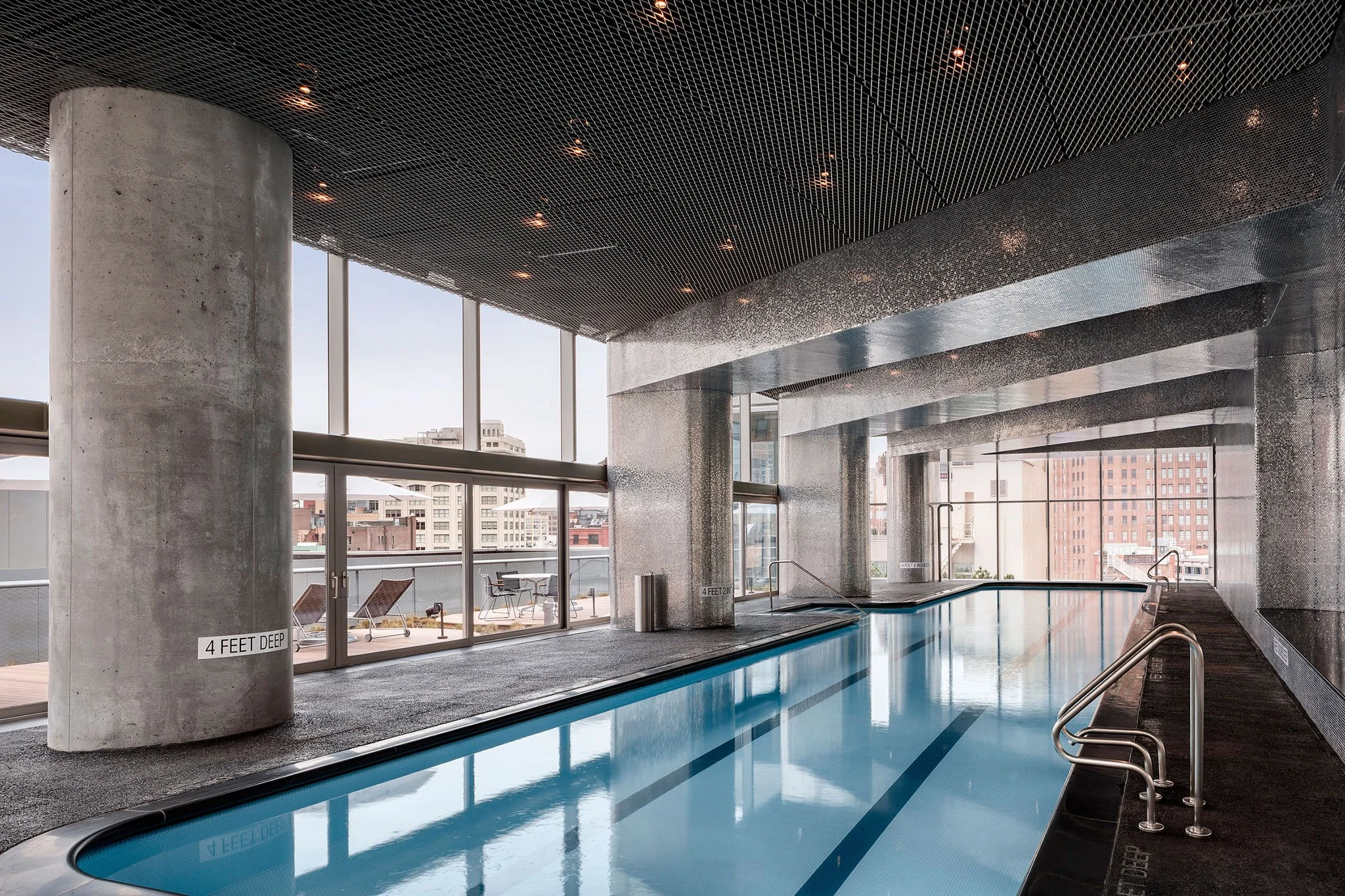 Indoor rooftop pool with large windows, urban city view, and modern concrete architecture.