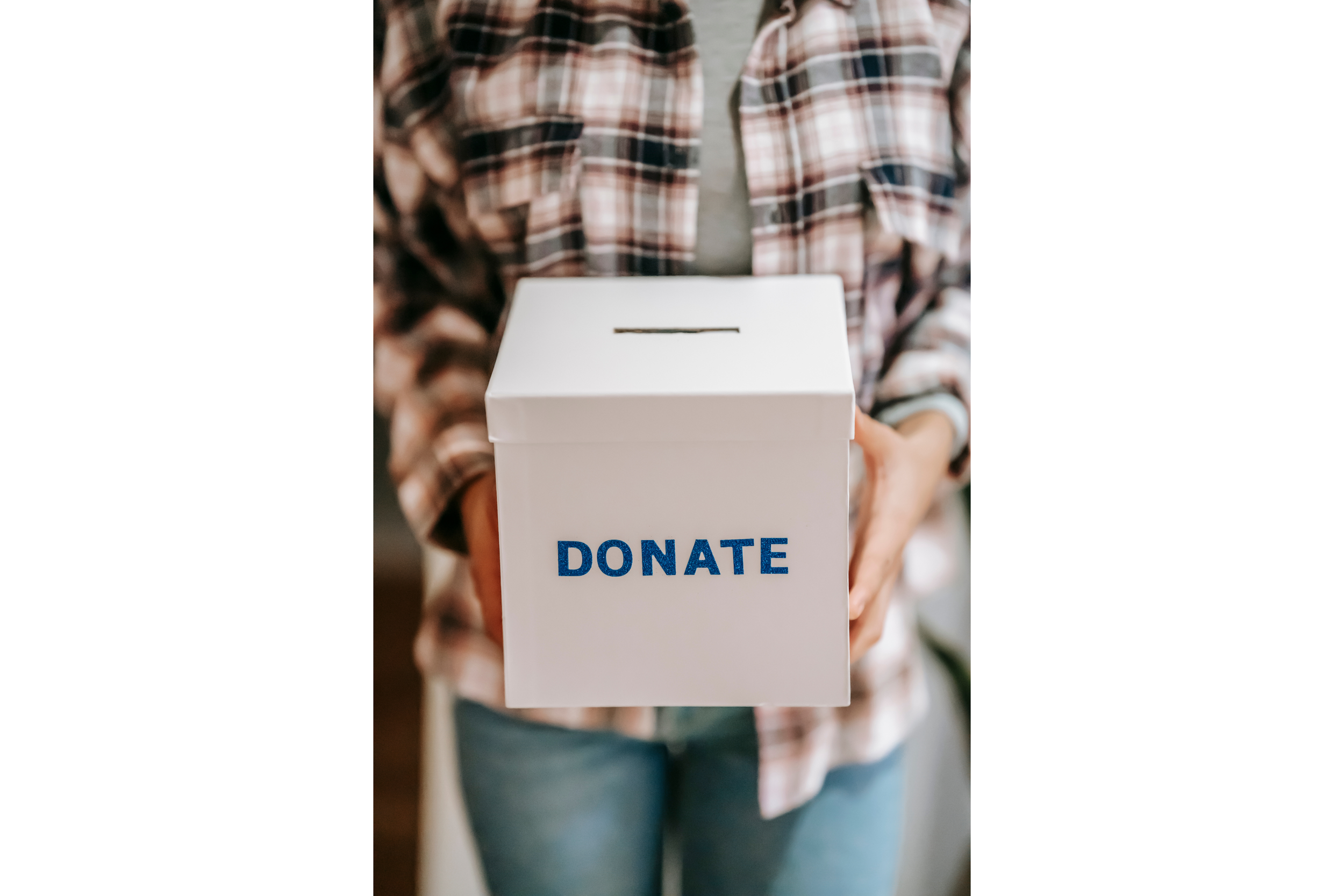 Person in plaid shirt holding a white donation box with 'DONATE' written in blue.