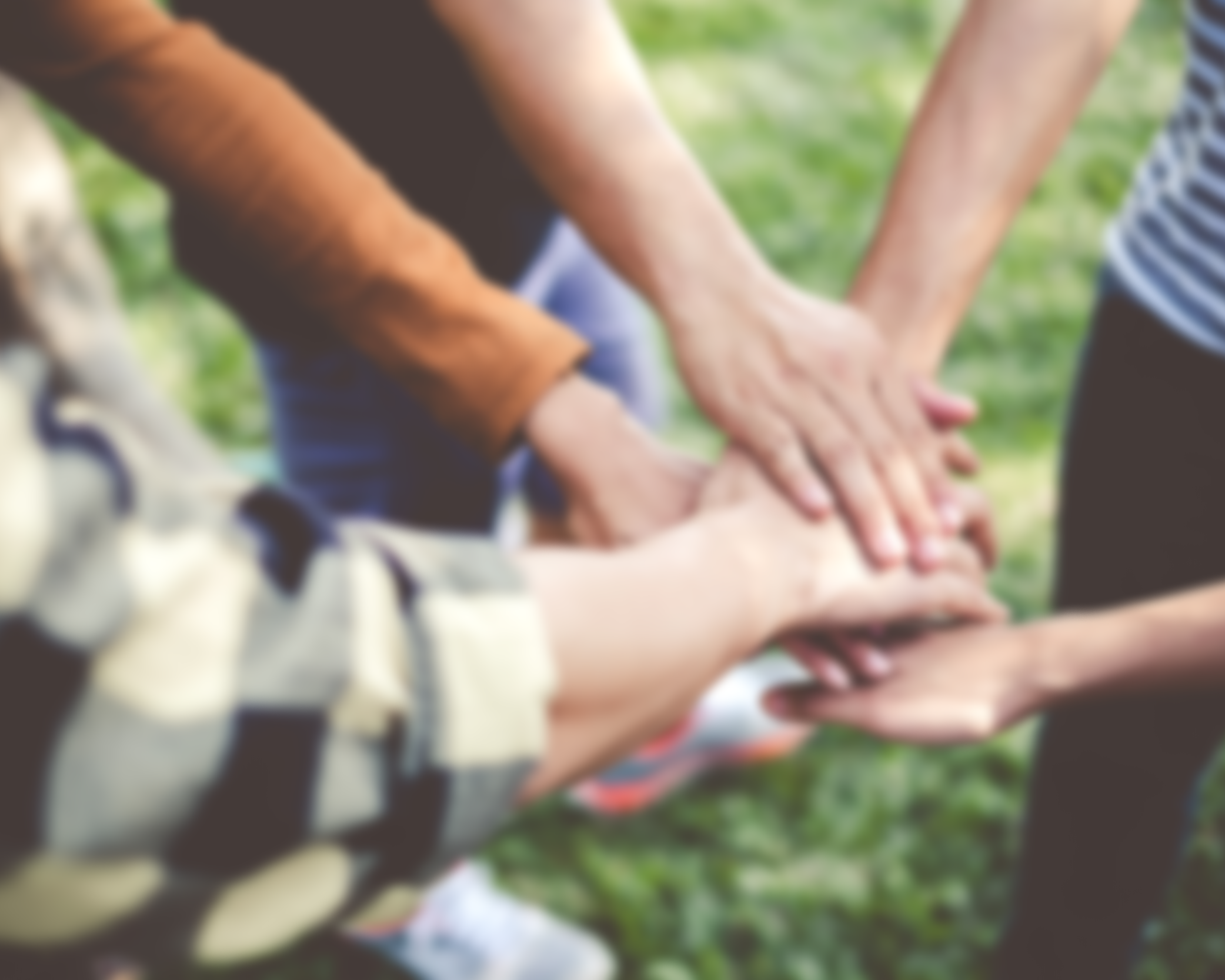 Volunteer for Brendan Moran's campaign. Multiple hands of different skin tones stacked together in a teamwork gesture outdoors on grass.