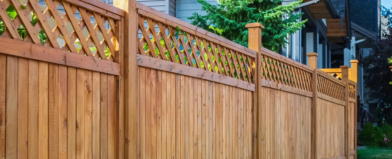 Wooden privacy fence with decorative lattice top, in a residential backyard with a house and trees in the background.