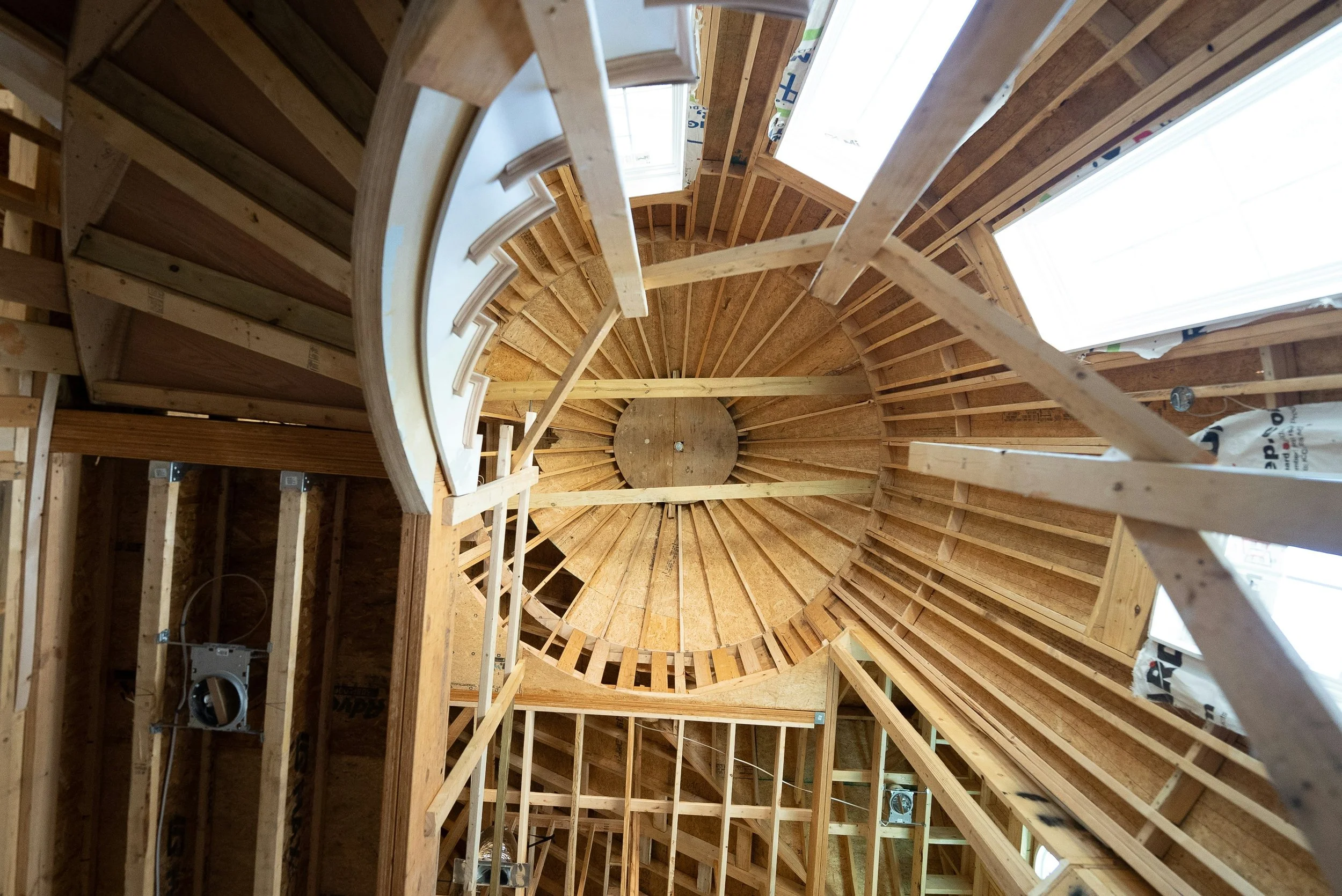 Looking up at the interior of a building under construction, showing a wooden spiral staircase and the framing of the walls and ceiling.