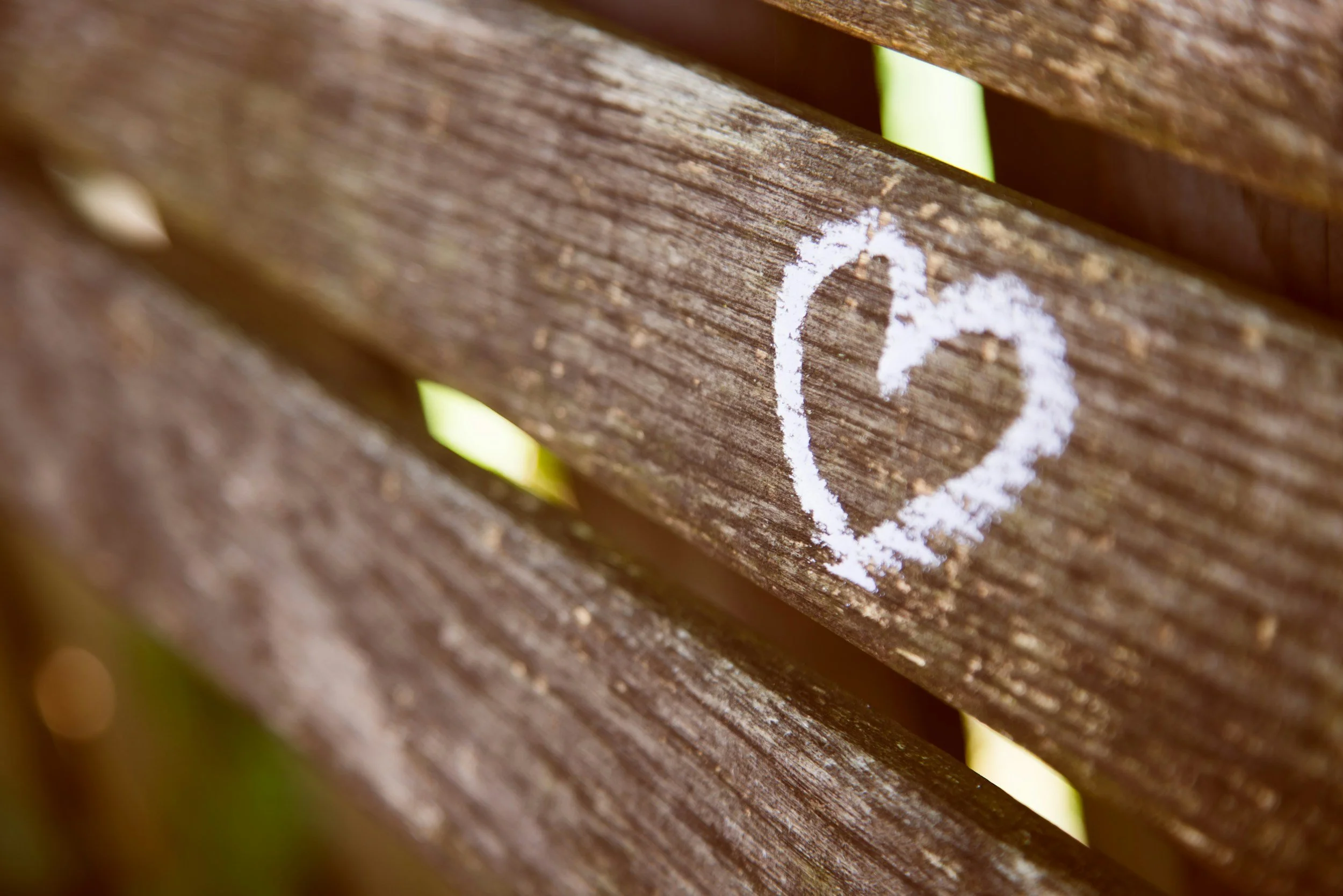 A close-up of a wooden bench with a white chalk heart drawn on it.