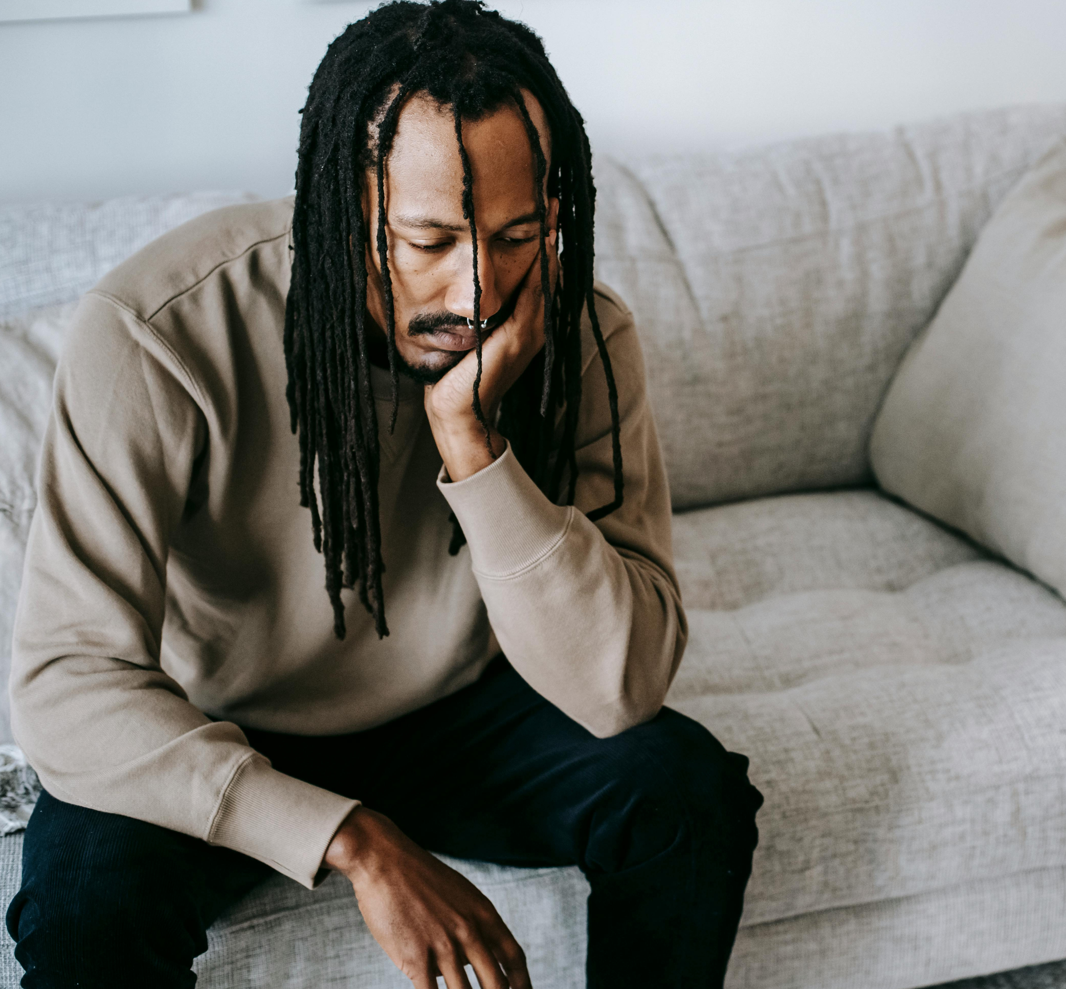 A man sitting on a beige sofa with his head resting on his hand, appearing contemplative or worried.