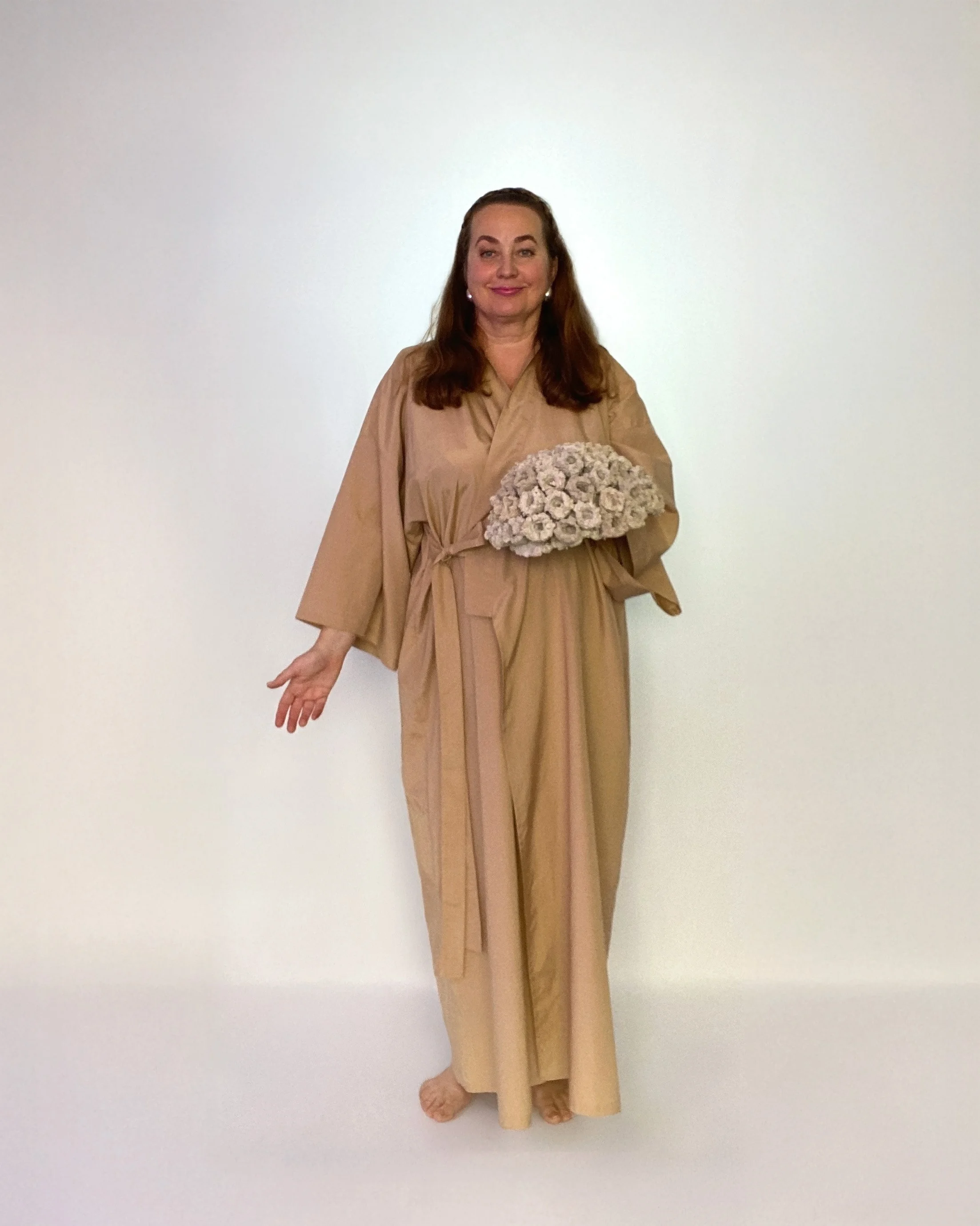Woman in beige traditional Japanese kimono holding a large bouquet of white flowers, standing against a plain white background.