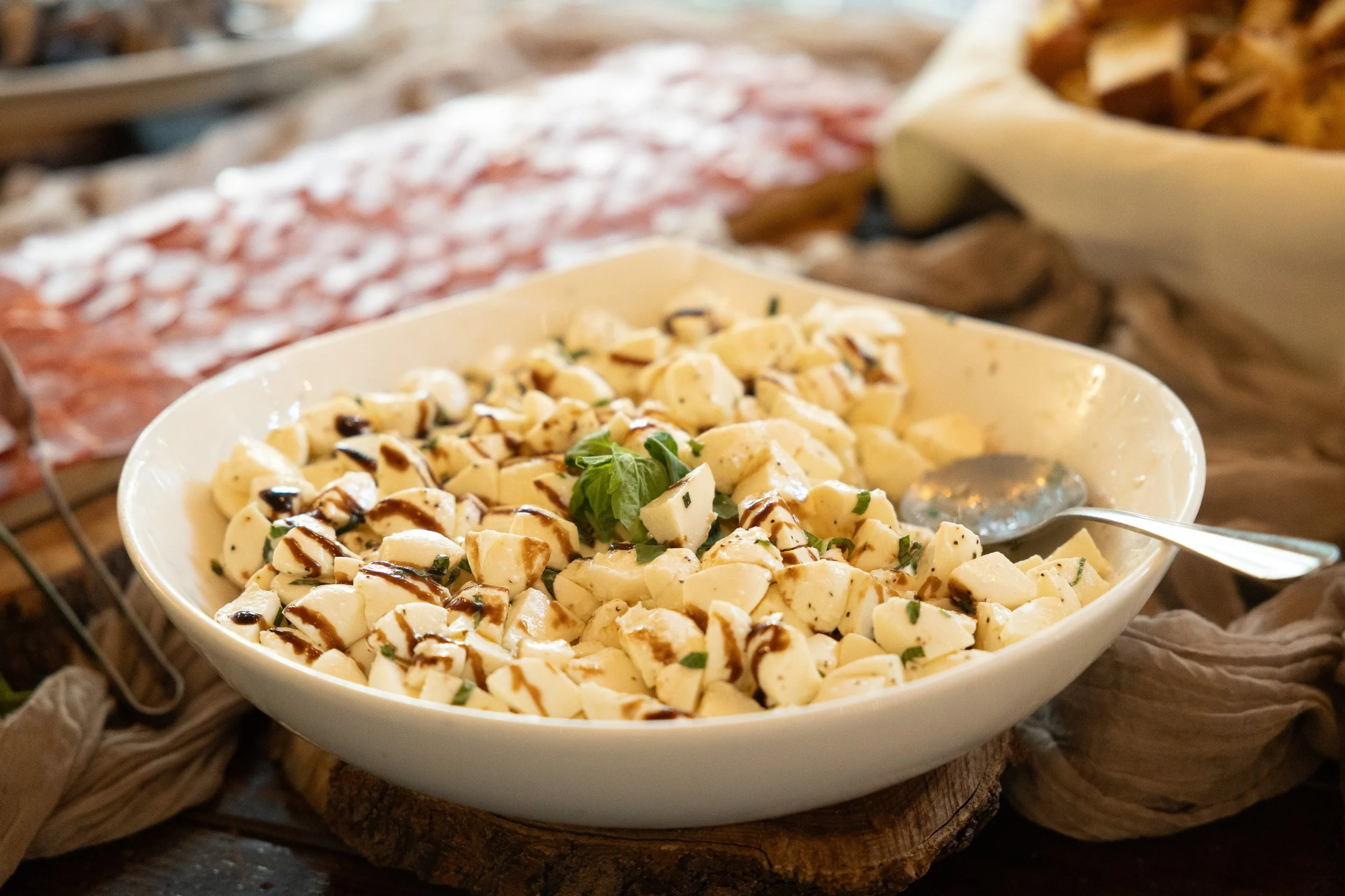 Bowls of cheese and cured meats on a wooden table at a buffet
