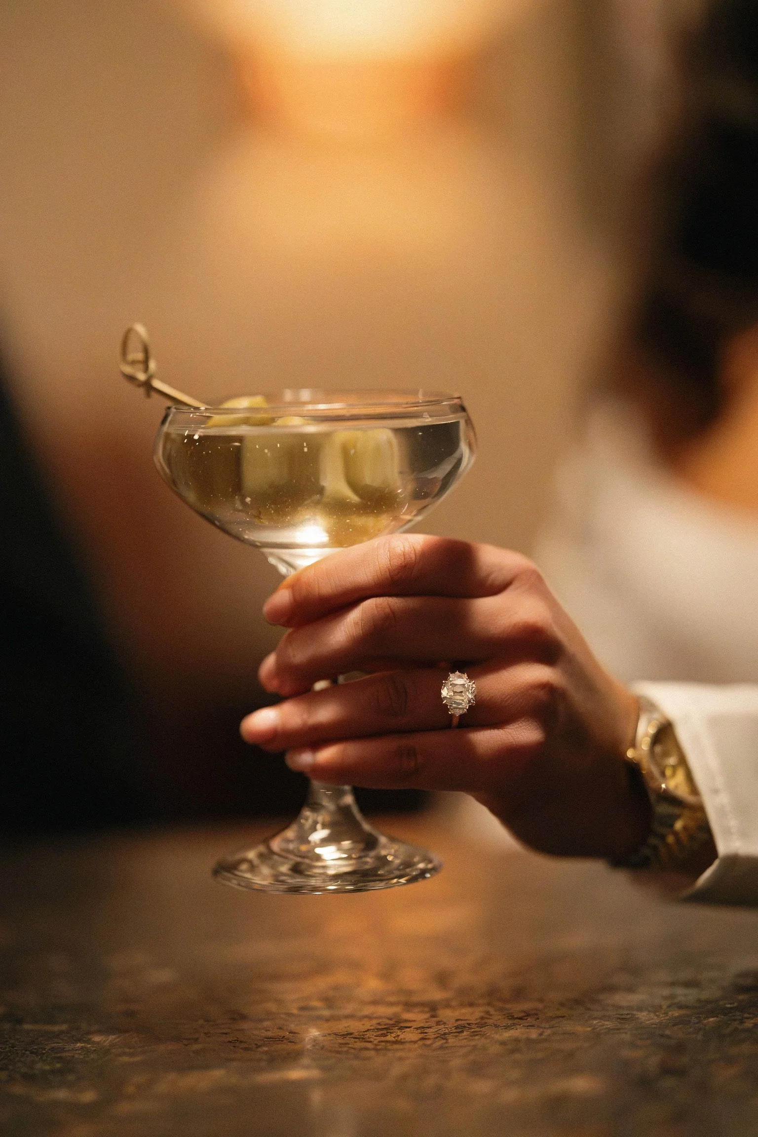 A person holding a cocktail glass with a white ring on their ring finger.
