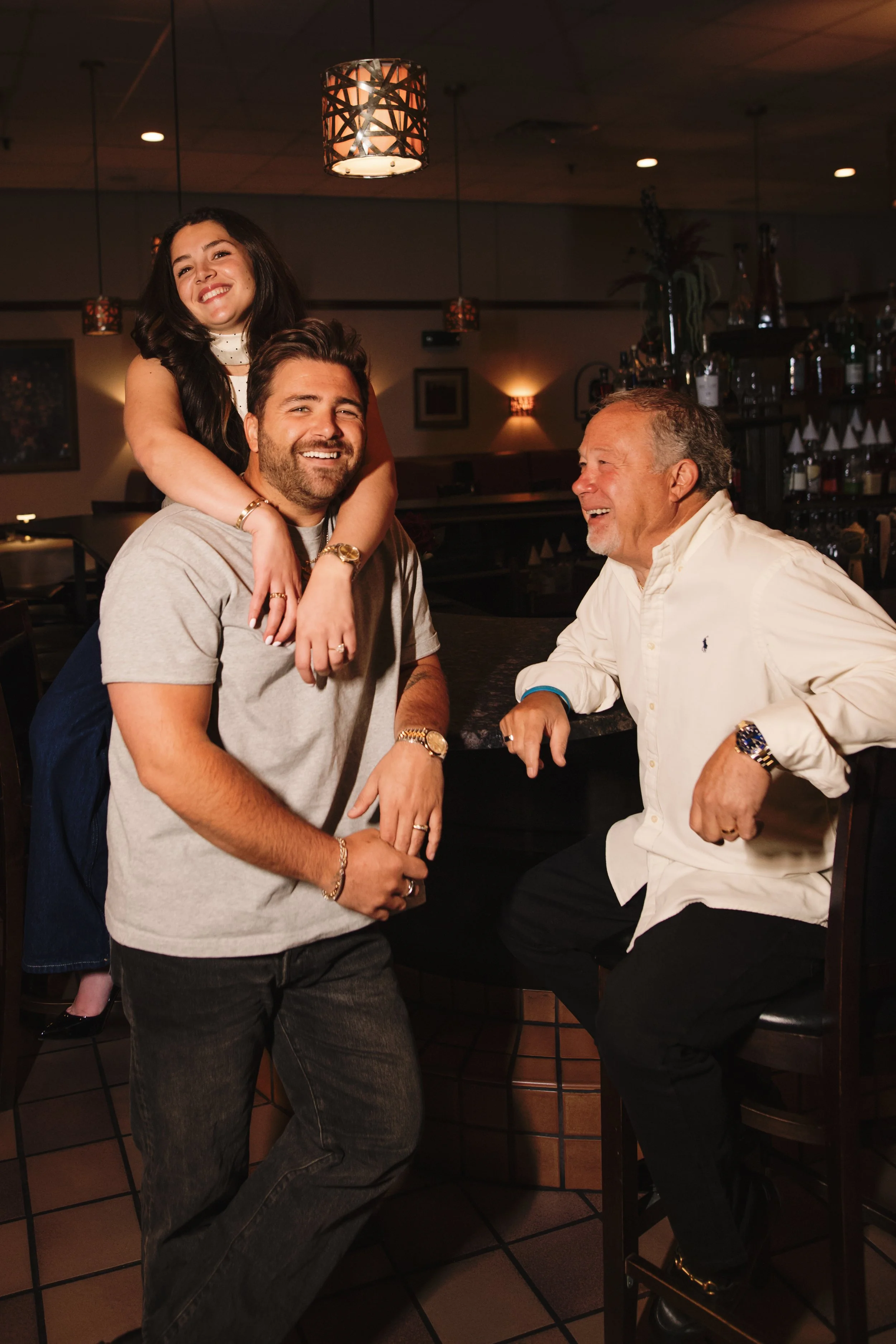 A family of four celebrating in a restaurant, with a young girl on a man's back, all smiling and enjoying their time together.