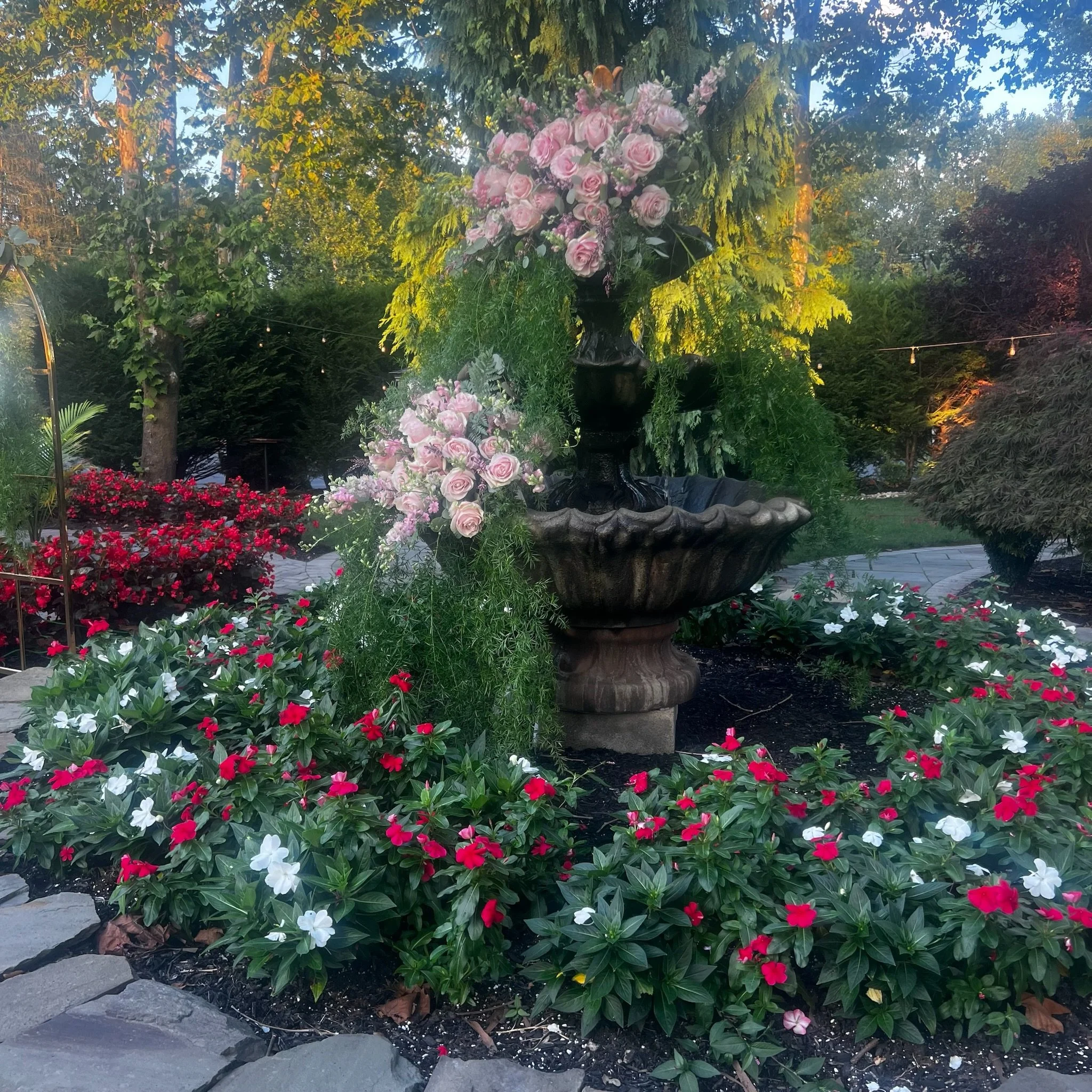 A garden fountain surrounded by colorful flowers and greenery in a well-maintained outdoor setting.