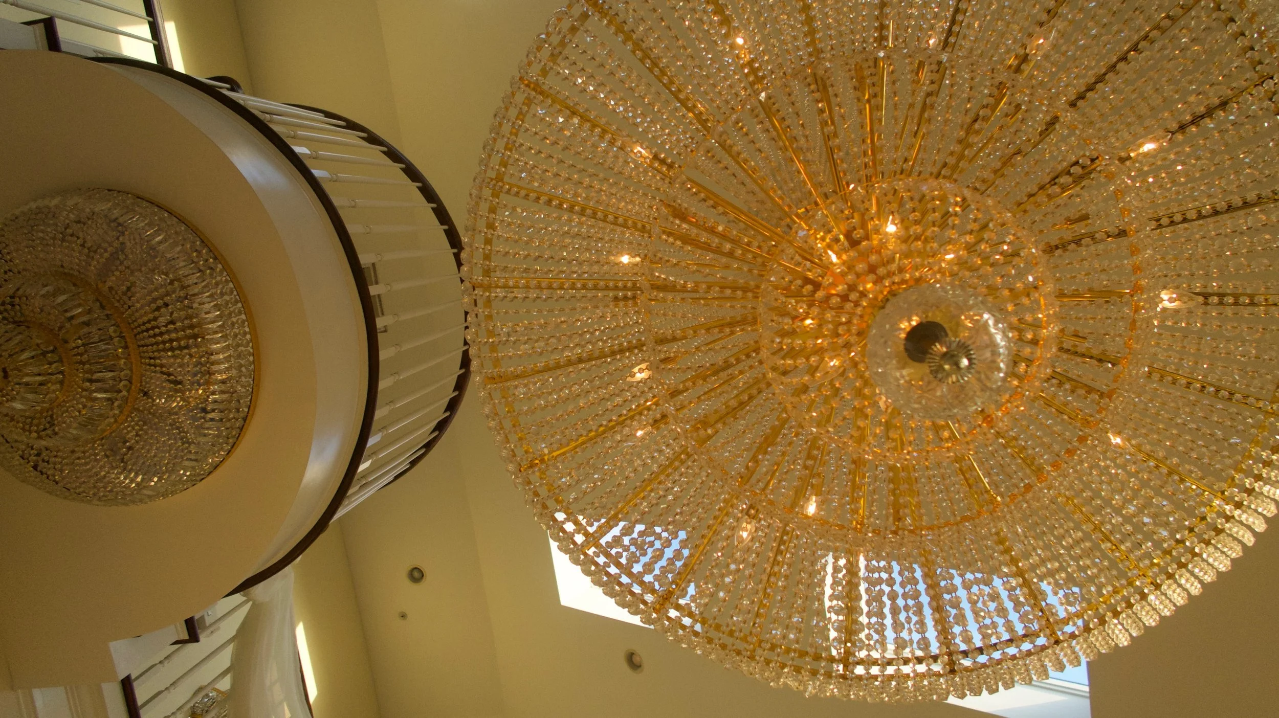 Close-up view of a large, ornate chandelier with numerous crystal beads and a smaller chandelier above it, hanging from a ceiling with a skylight.