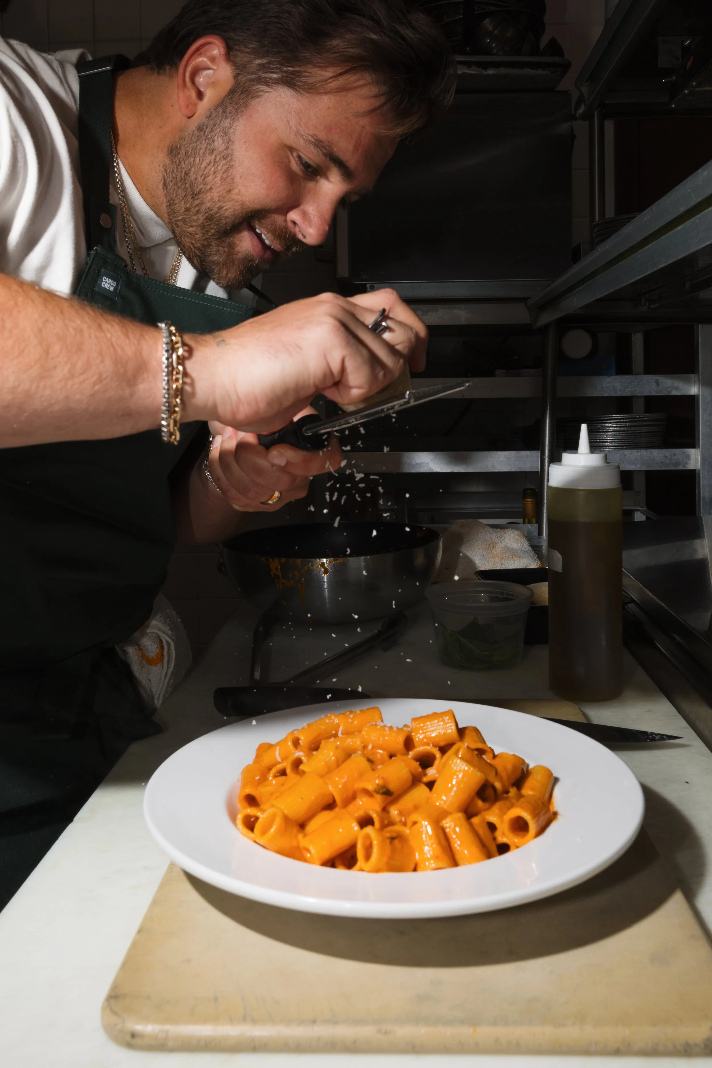 A chef seasoning a plate of pasta in a kitchen.