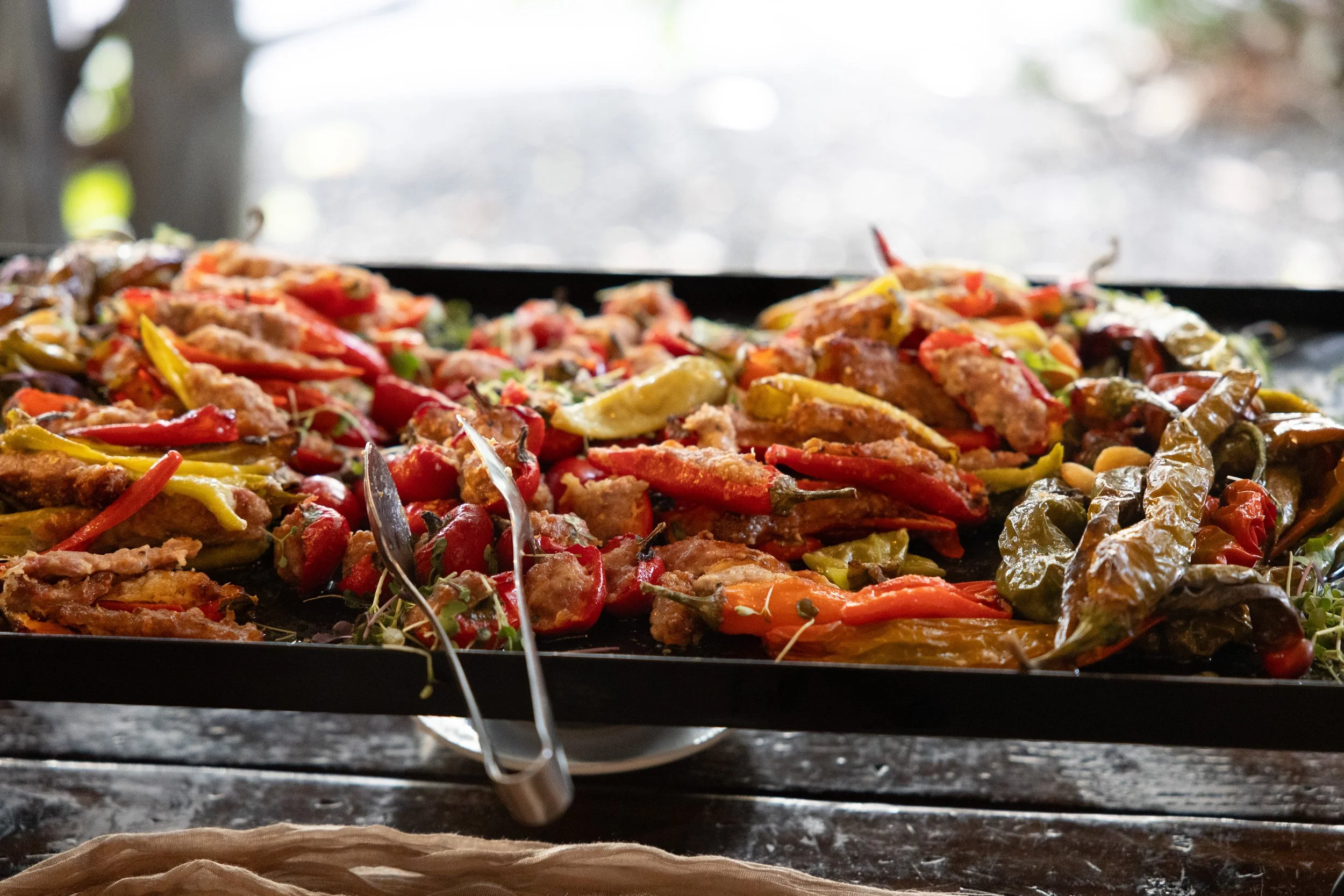 Assorted roasted peppers on a serving tray with tongs.