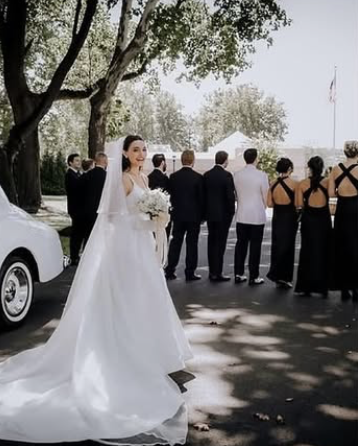 Bride in a wedding dress standing outdoors with guests in the background.