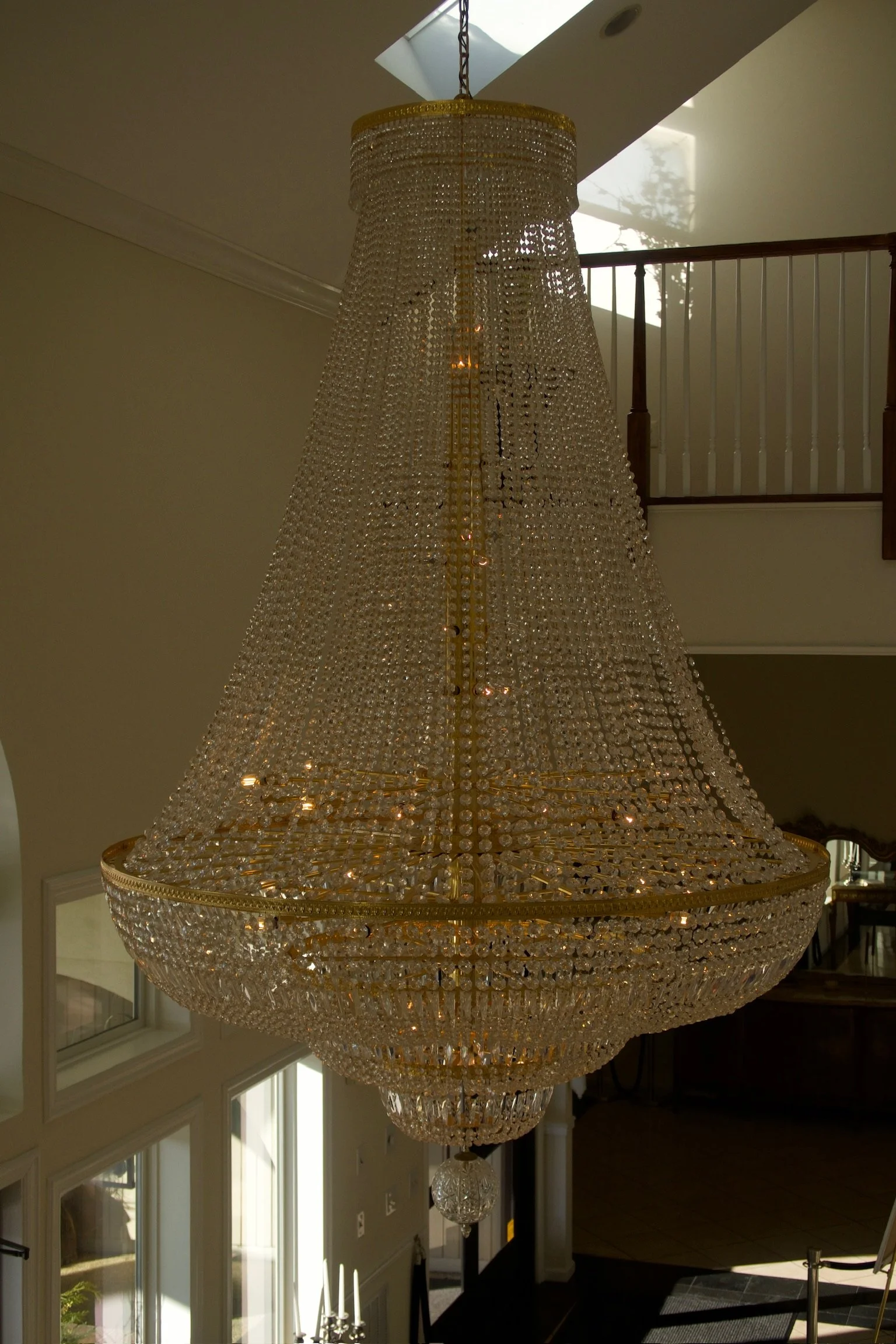 Large crystal chandelier hanging from ceiling in a spacious room with tall windows.