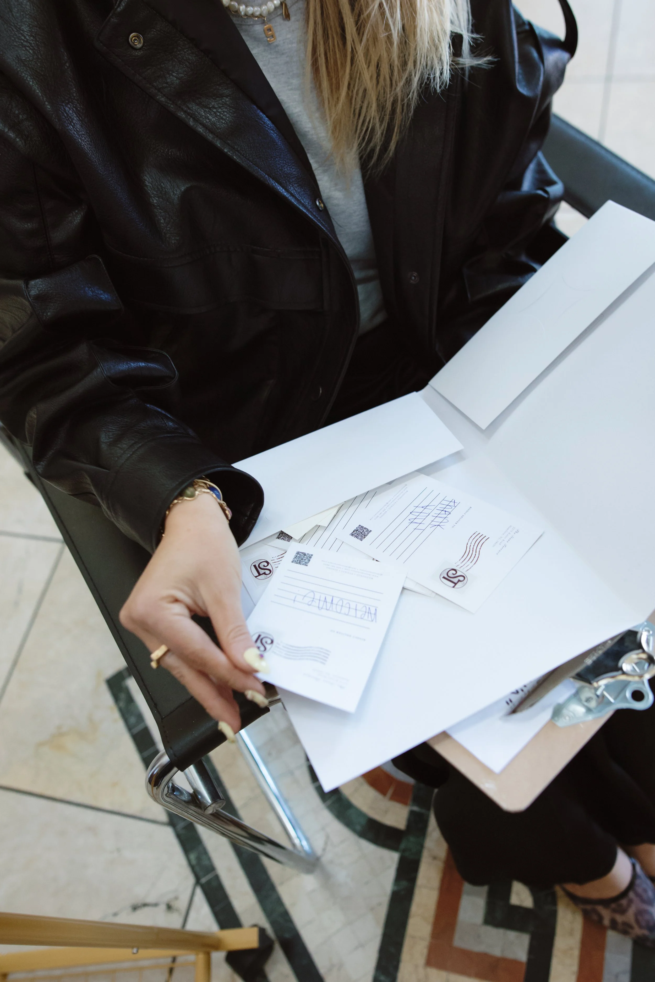 Person wearing a black leather jacket handling postal envelopes and papers at a table.