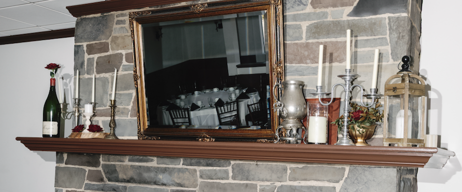 Decorative fireplace mantel with a mirror, candles, a bottle, and a lantern.