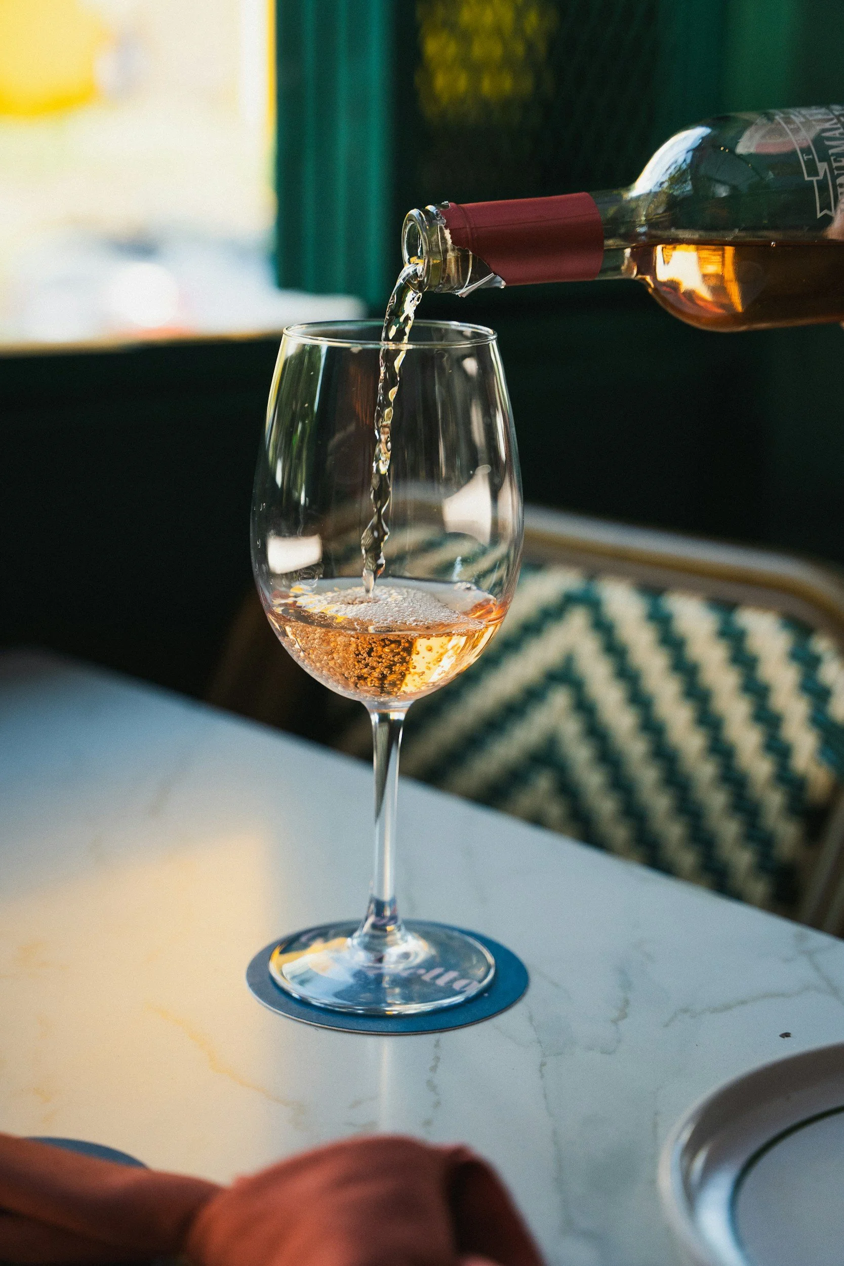 A glass of rosé wine on a table with a bottle pouring wine into it.