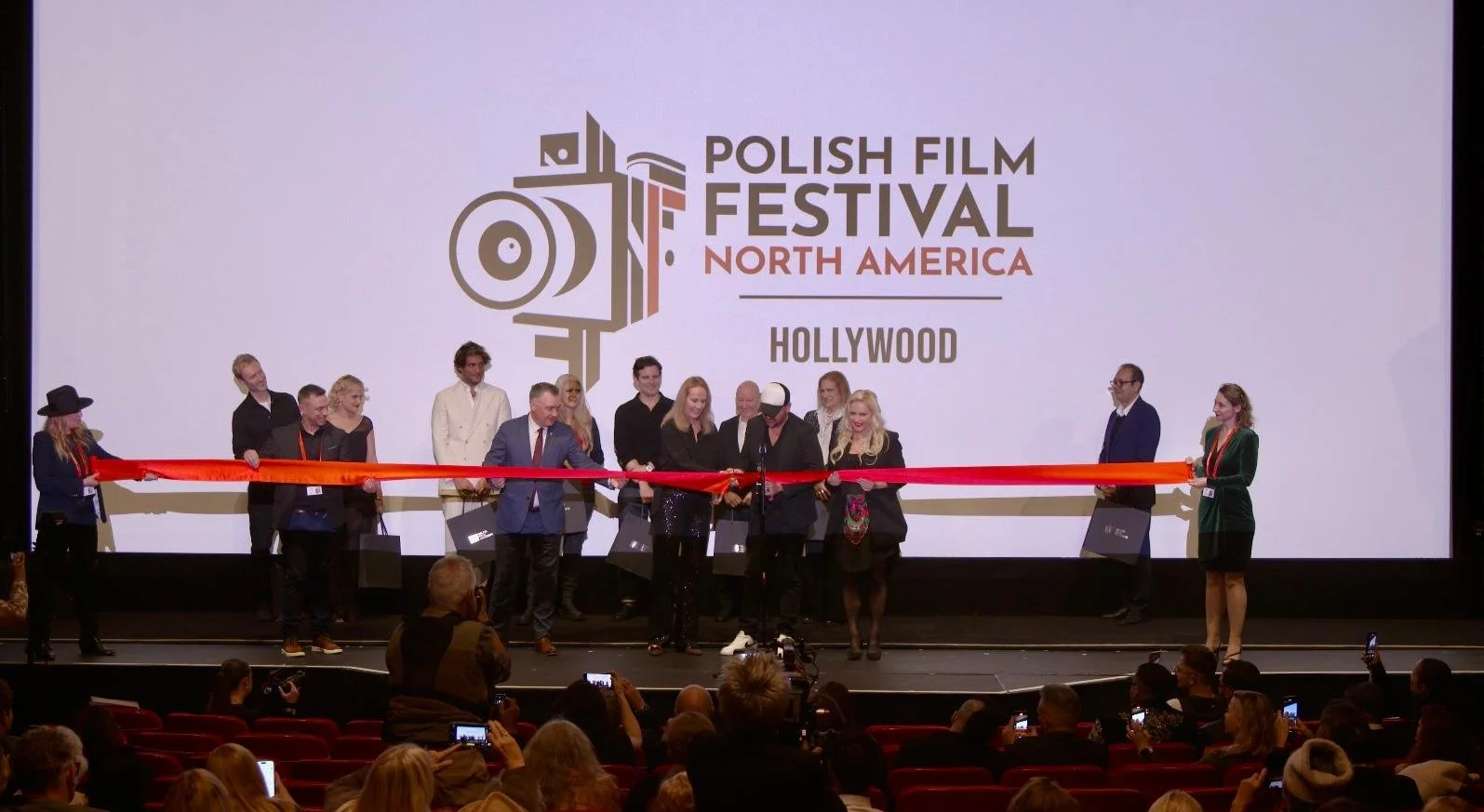 Group of people on stage at the Polish Film Festival North America in Hollywood, participating in a ribbon-cutting ceremony.