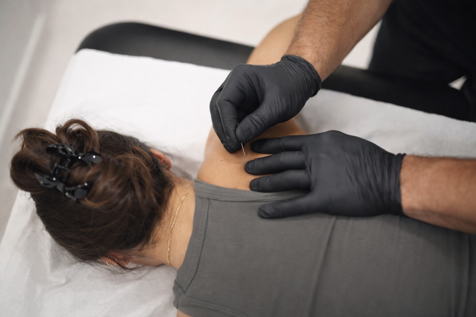 A physical therapist is helping a woman with shoulder pain or injury, demonstrating treatment or therapy exercises in a clinical setting.