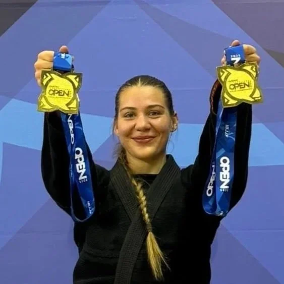 Female athlete in martial arts uniform holding two medals with a blue background.