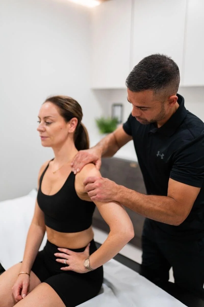 A woman receiving shoulder therapy from a man in a clinical setting.