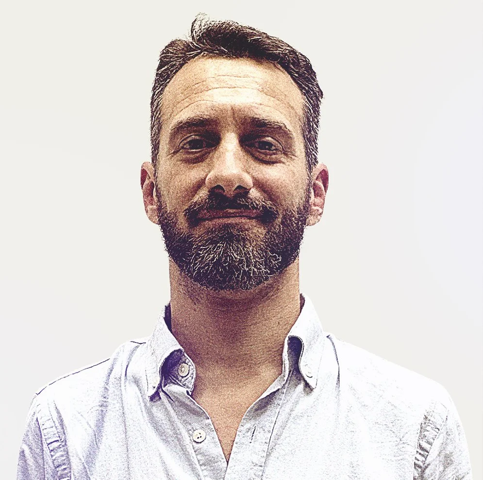 Retrato de un hombre con barba y cabello oscuro, usando una camisa blanca, en un fondo blanco.