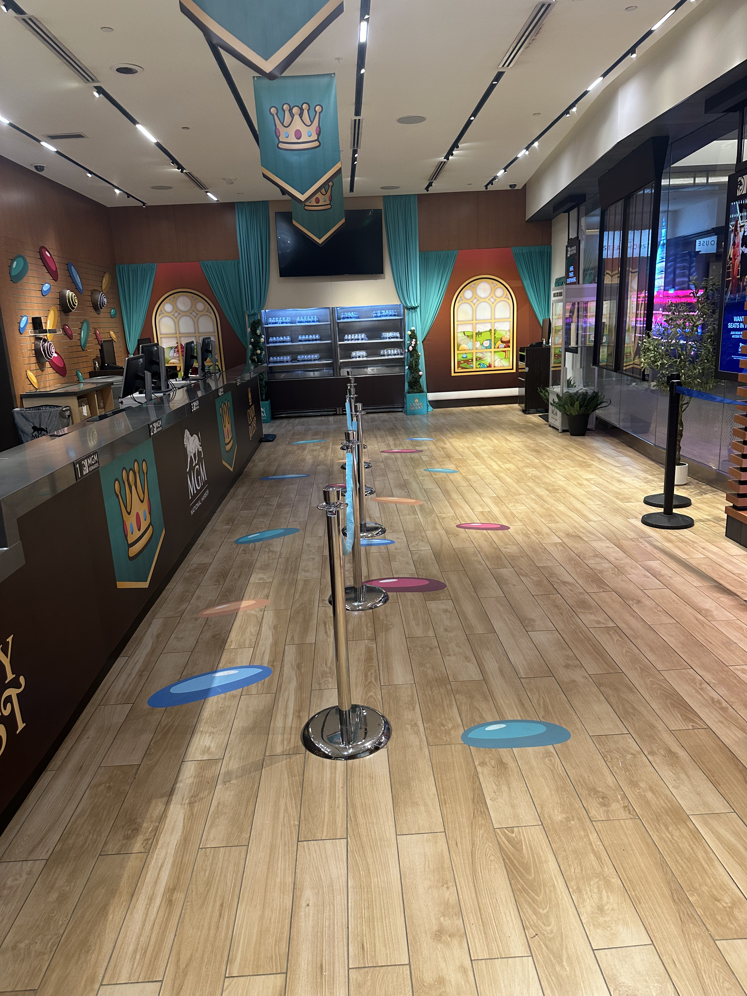 Inside an empty indoor entertainment center or arcade with check-in counters, colorful wall decorations, teal curtains, and floor stickers for social distancing.