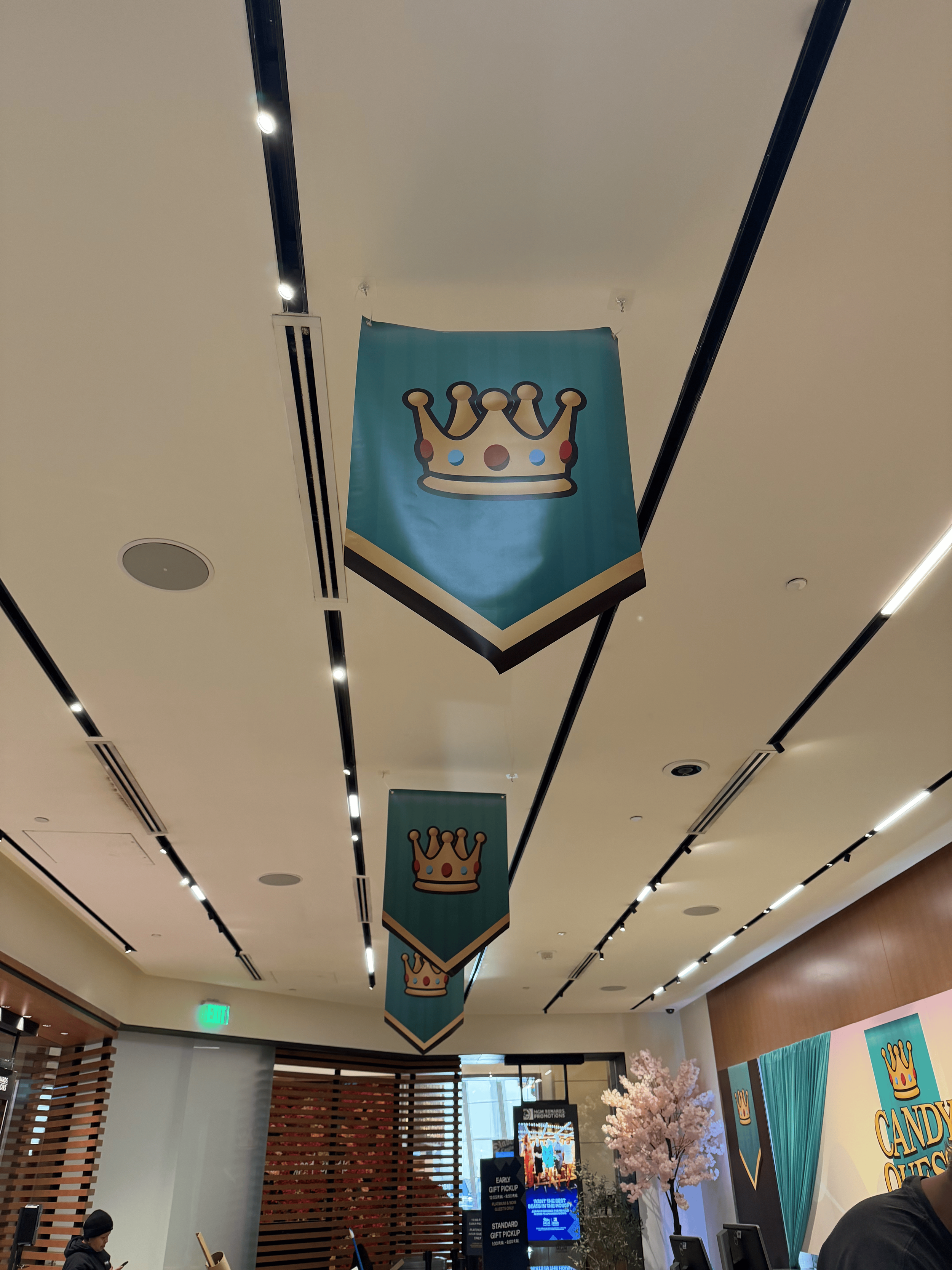 Indoor shopping area with hanging banners featuring a crown logo, pink cherry blossom trees, and a promotional sign for Candy Crush.