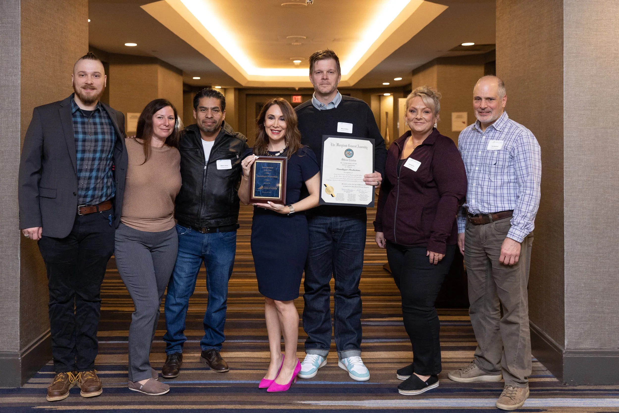 Group of seven people standing in a hallway, holding awards and certificates, celebrating an achievement.