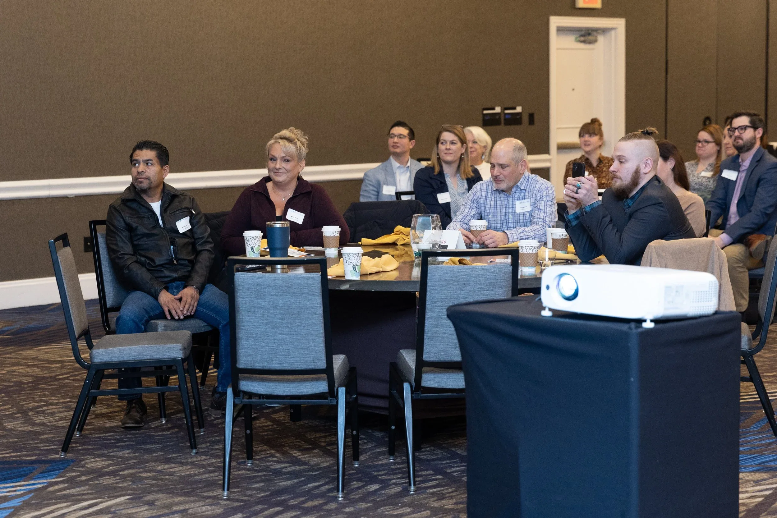 People seated around a round table at a conference or seminar, with a projector in the foreground.