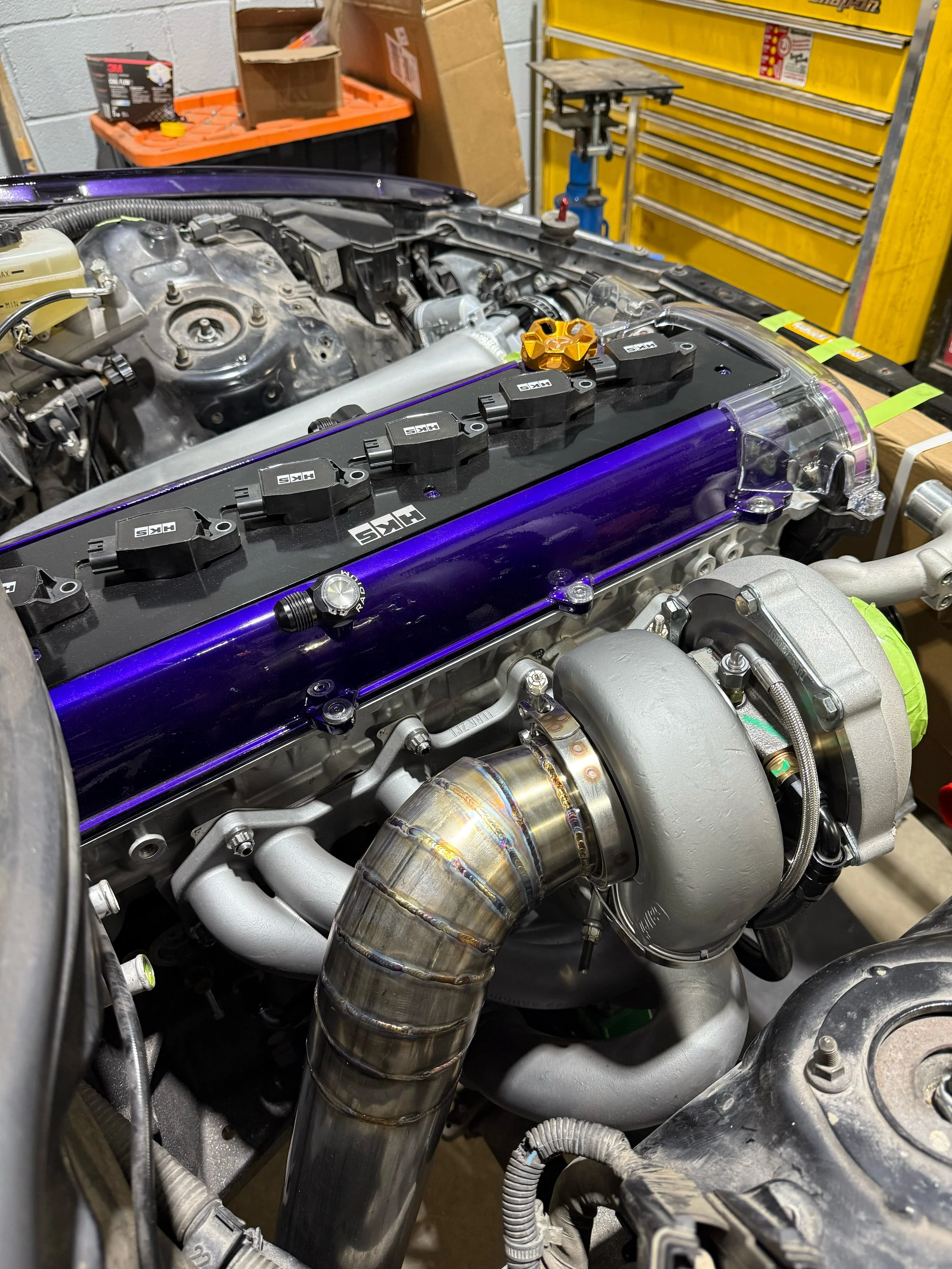 Close-up of a turbocharged car engine with visible piping and ignition coils, in a workshop setting.