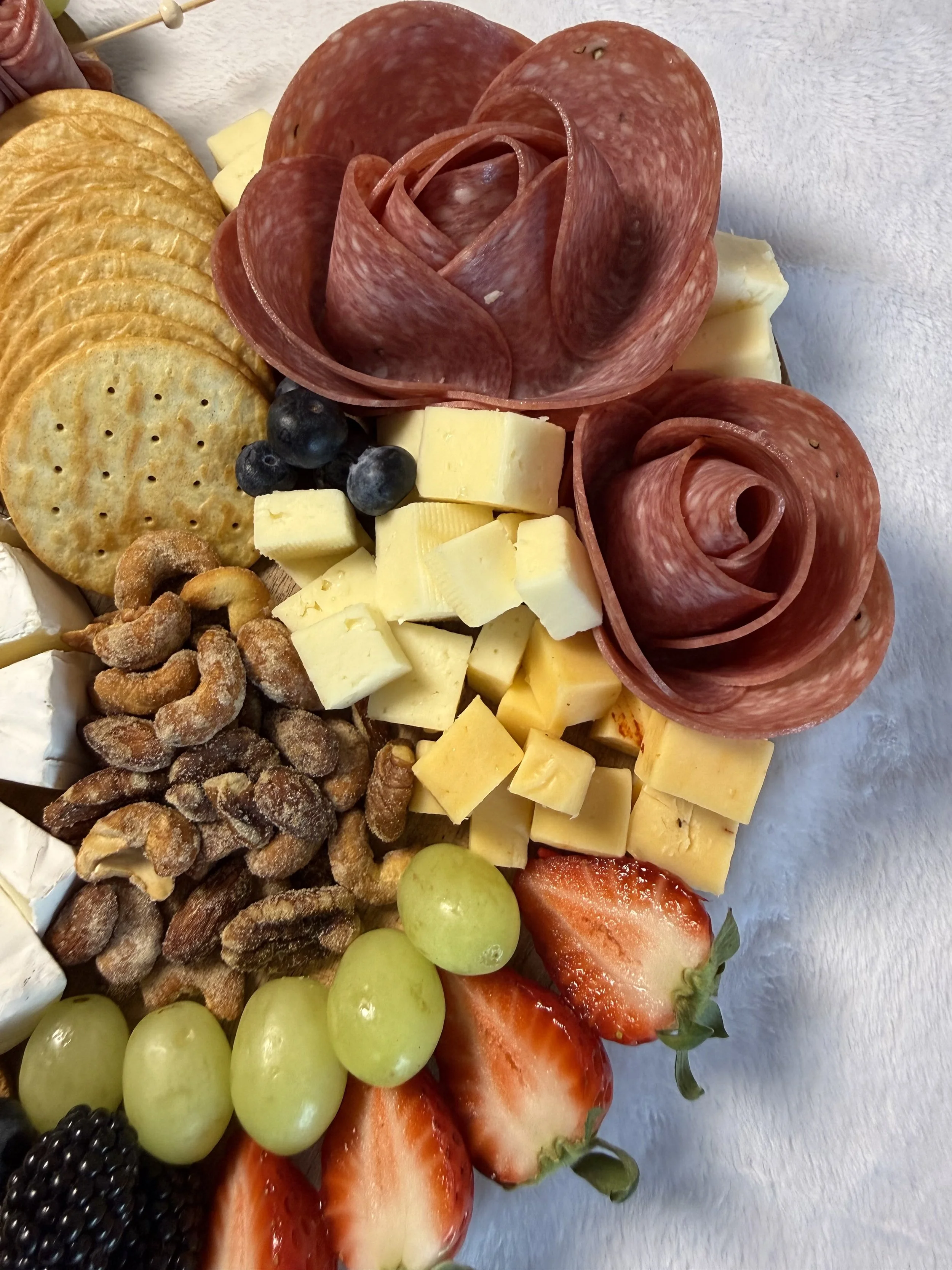 Cheese, strawberries, grapes, nuts, crackers, blueberries, blackberries, and sliced meats arranged on a platter.