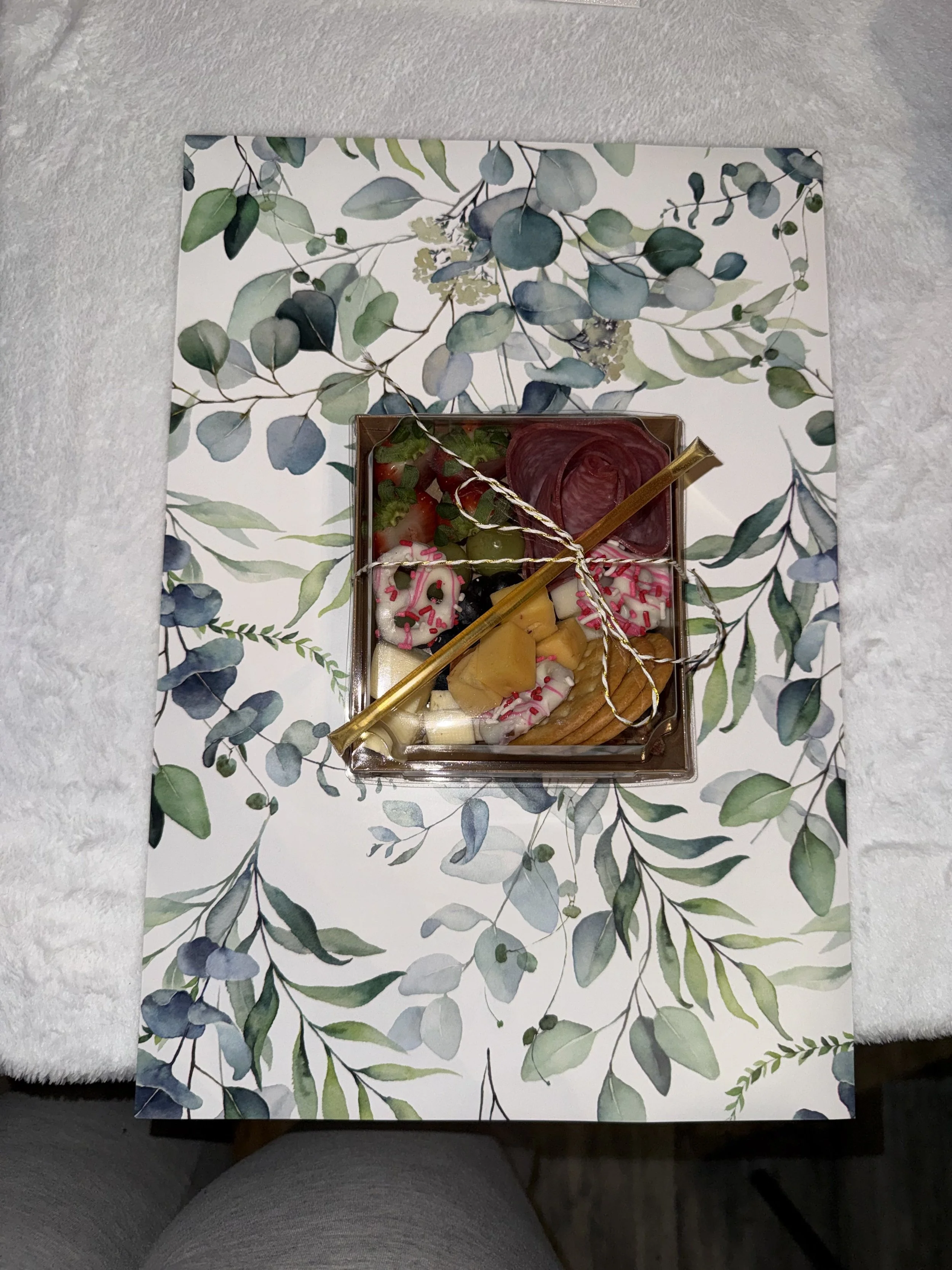 A box of assorted decorated cookies with pink sprinkles, pineapple chunks, and other toppings on a floral-patterned tray.
