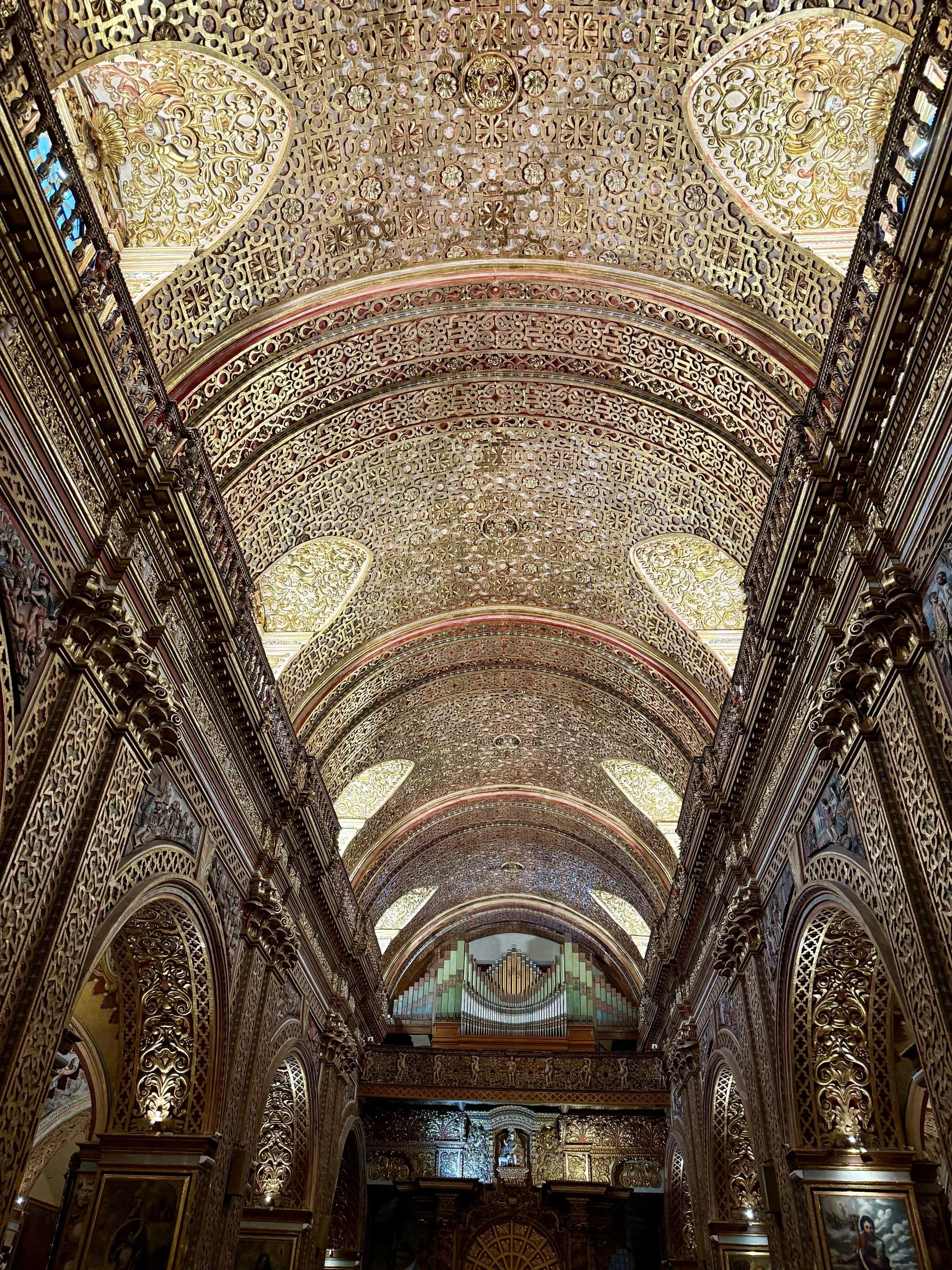 Ornately decorated church interior with gold accents, arched ceilings, and a pipe organ at the far end.
