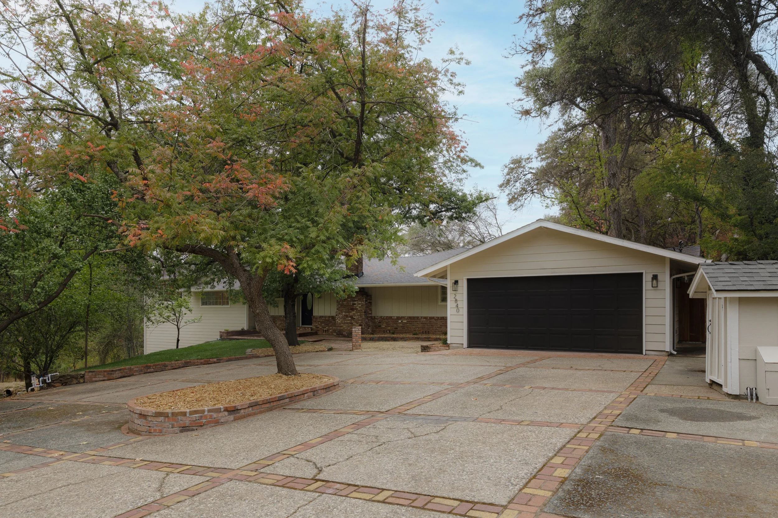 Tree-lined suburban home with a two-car garage, brick accents, and a broad concrete driveway.
