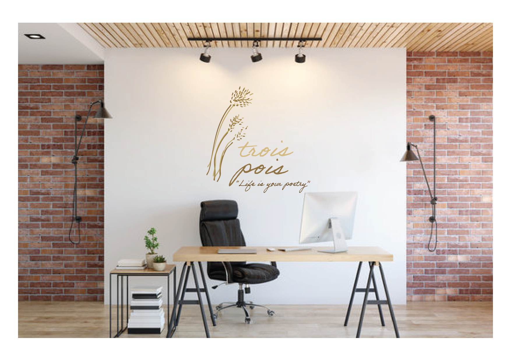 Office space with brick and white walls, desk with a computer, black office chair, and wall art reading 'trois peux' with a quote 'Life is your poetry,' and decorative plants.