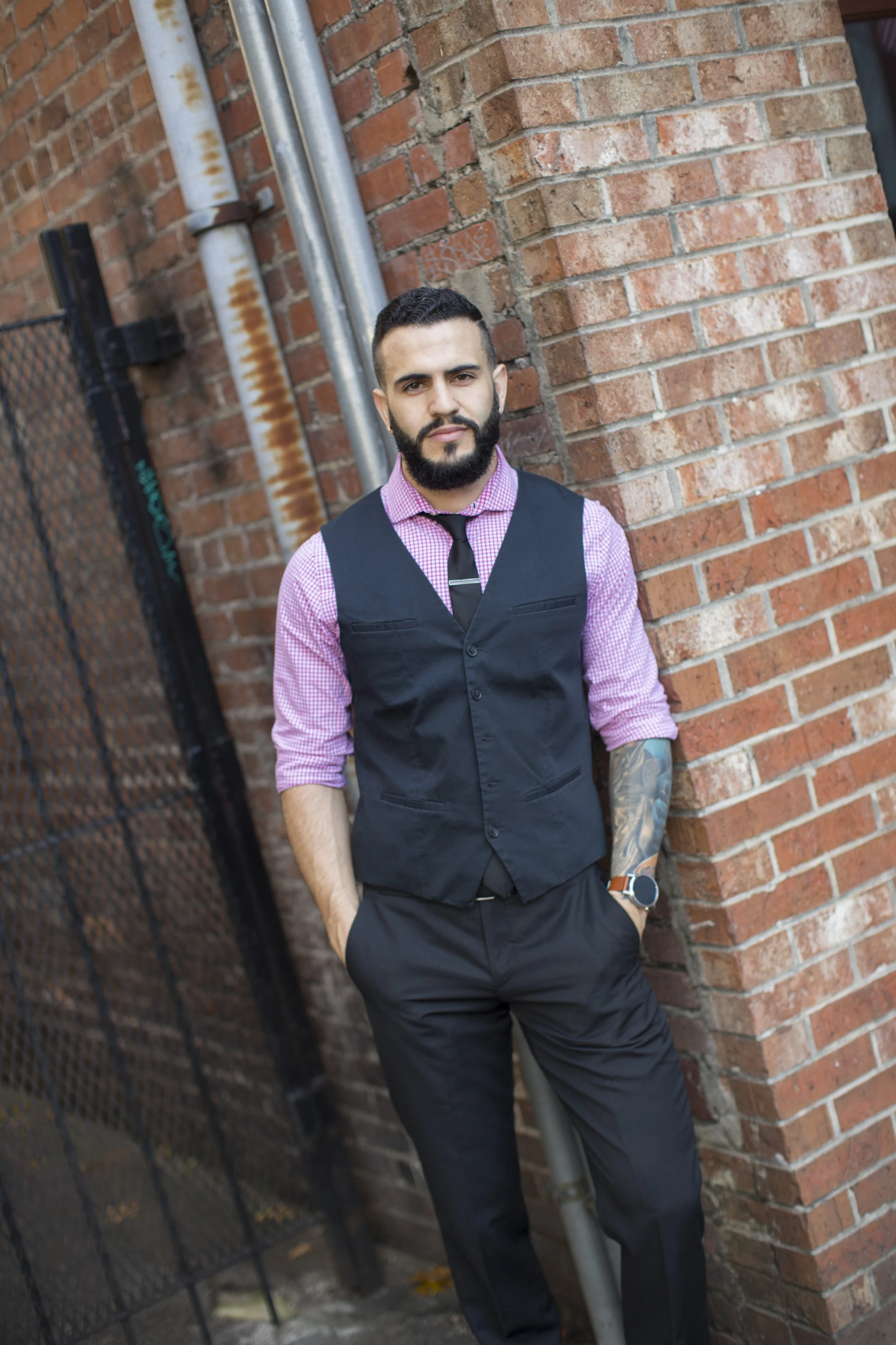 a well dressed business man standing in front of a brick wall with his hands in his pockets