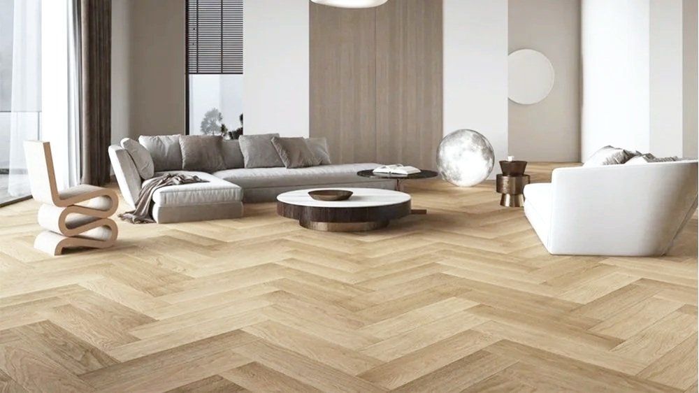 Modern living room with a light wood herringbone floor, a large gray sectional sofa, a white armchair, small wooden side tables, decorative moon lamp, and abstract wall decor.